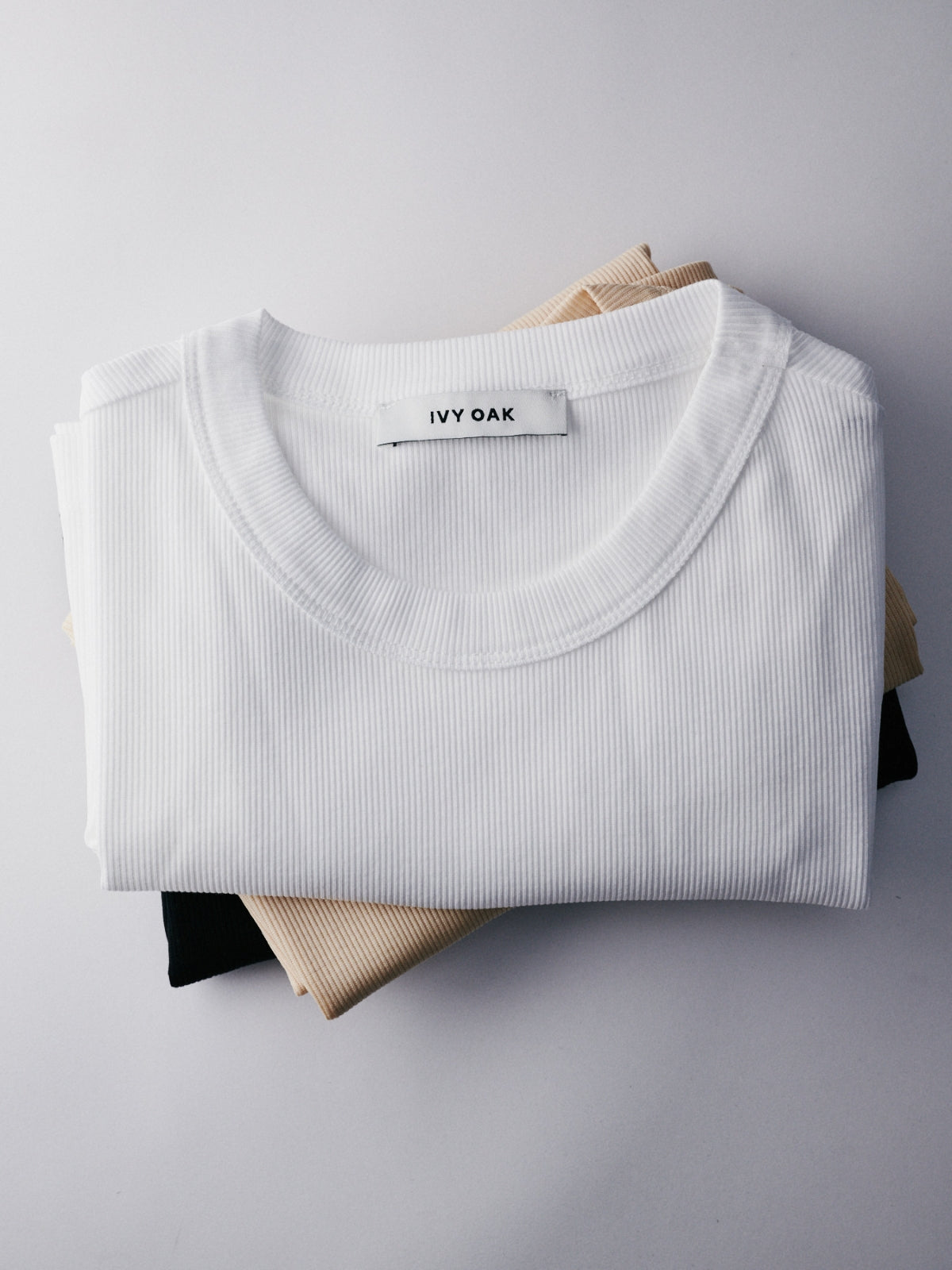 A white Ivy Oak t-shirt folded neatly on top of beige and black shirts against a white background.