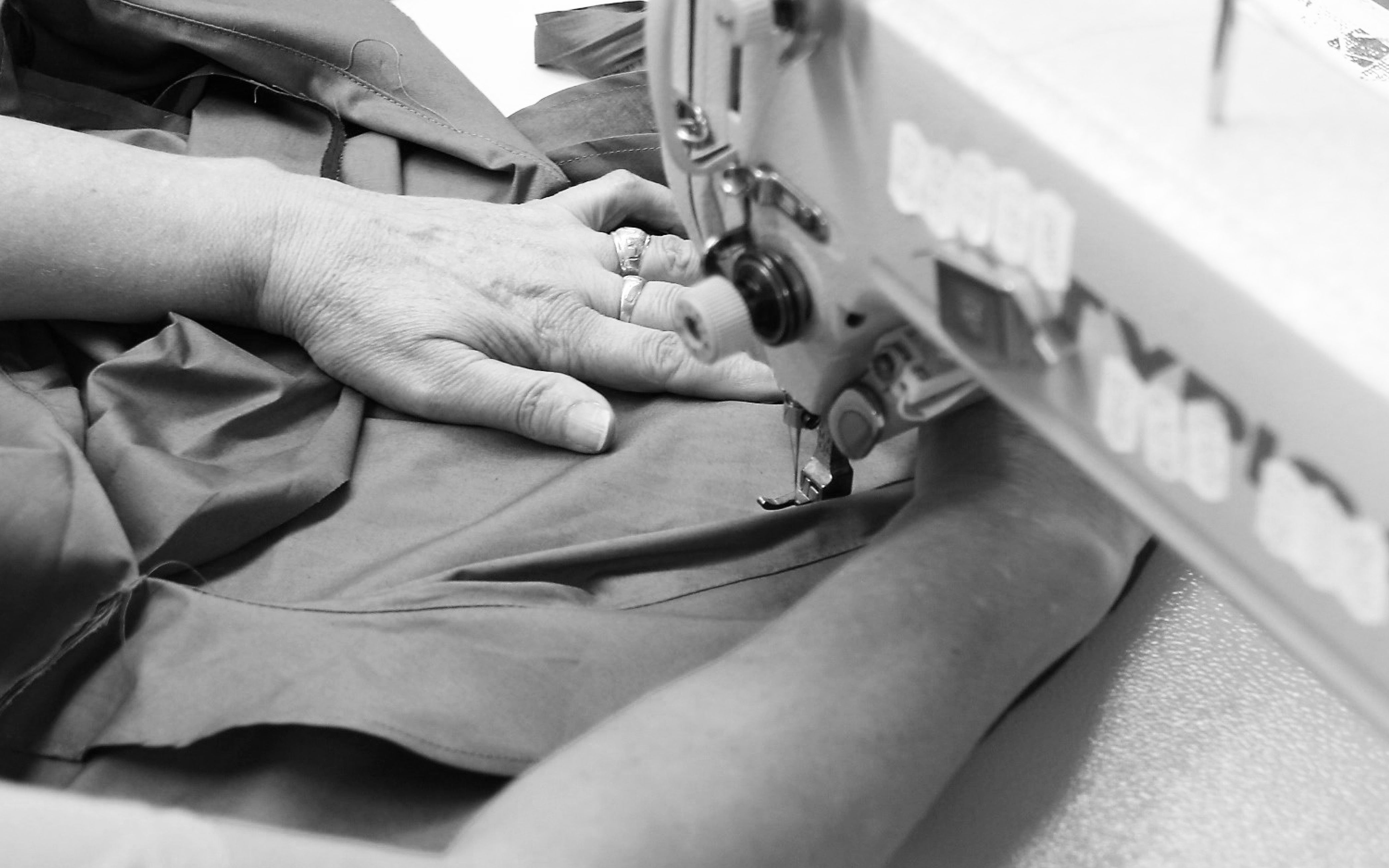 Close-up of hands guiding fabric through a sewing machine in black and white.