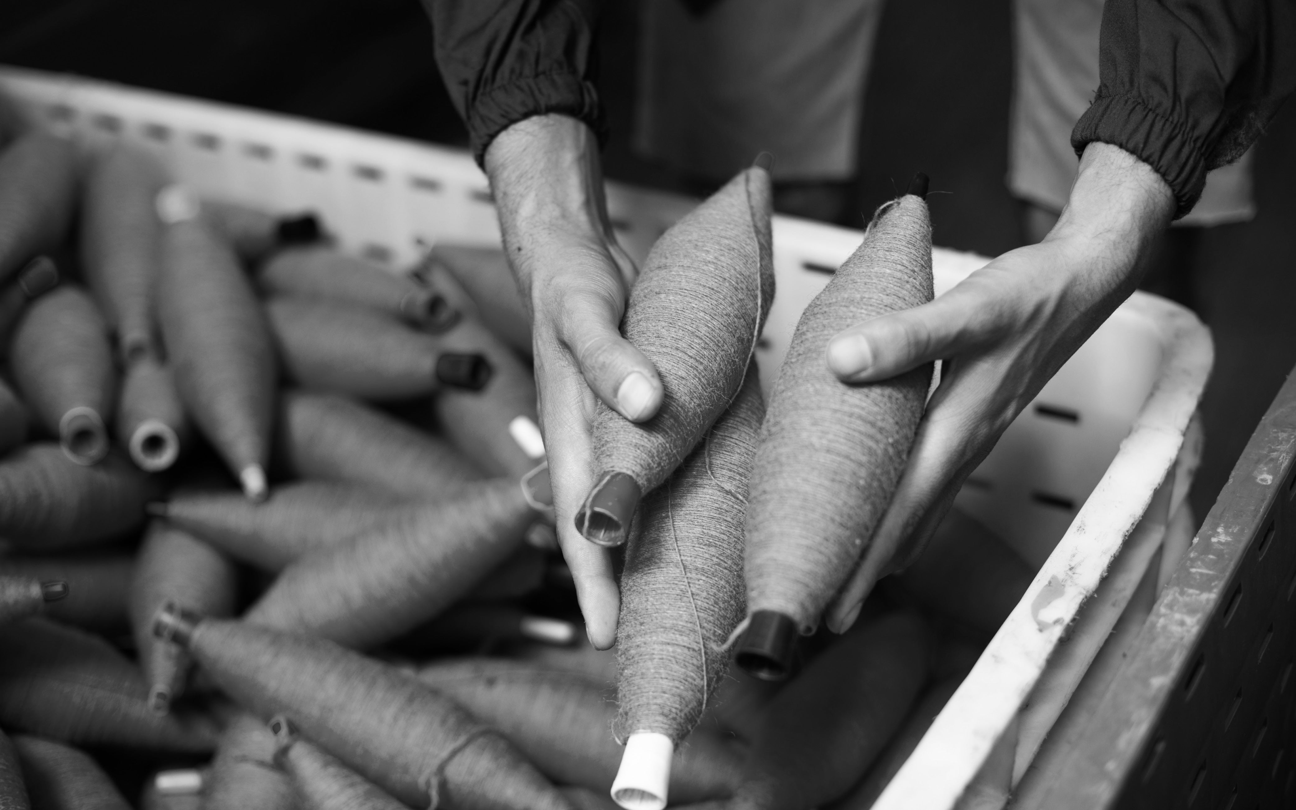 Hands holding yarn spools over a bin filled with more yarn spools in black and white.