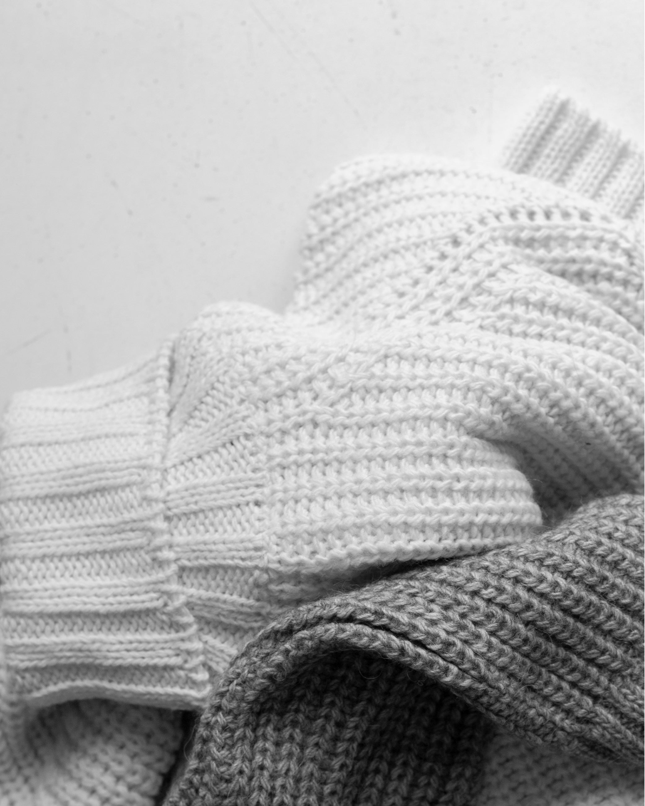 Folded knitted sweaters in white and gray lying on a white surface, shown in a close-up view.