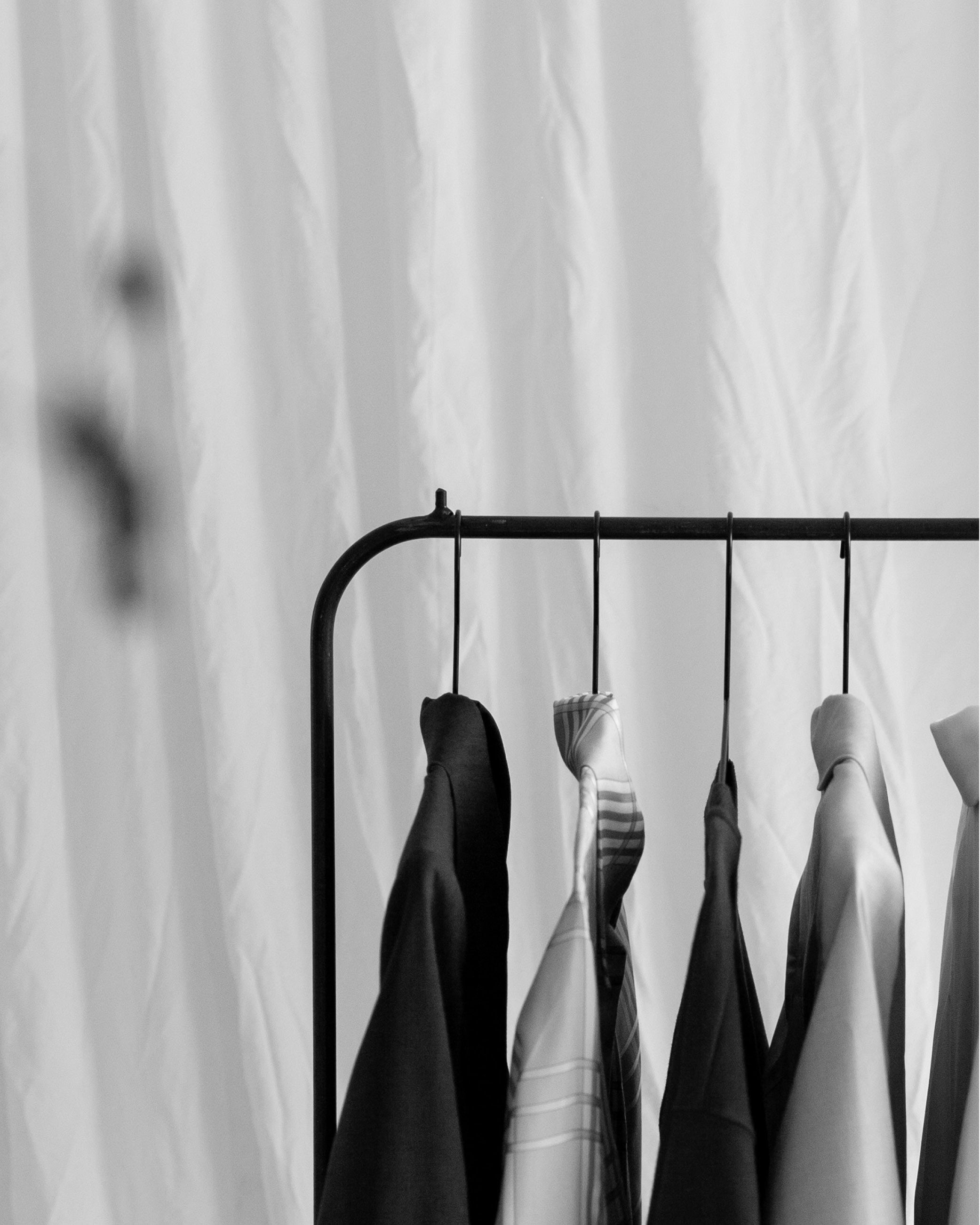 Black and white photo of clothes hanging on a rack in front of a curtain.