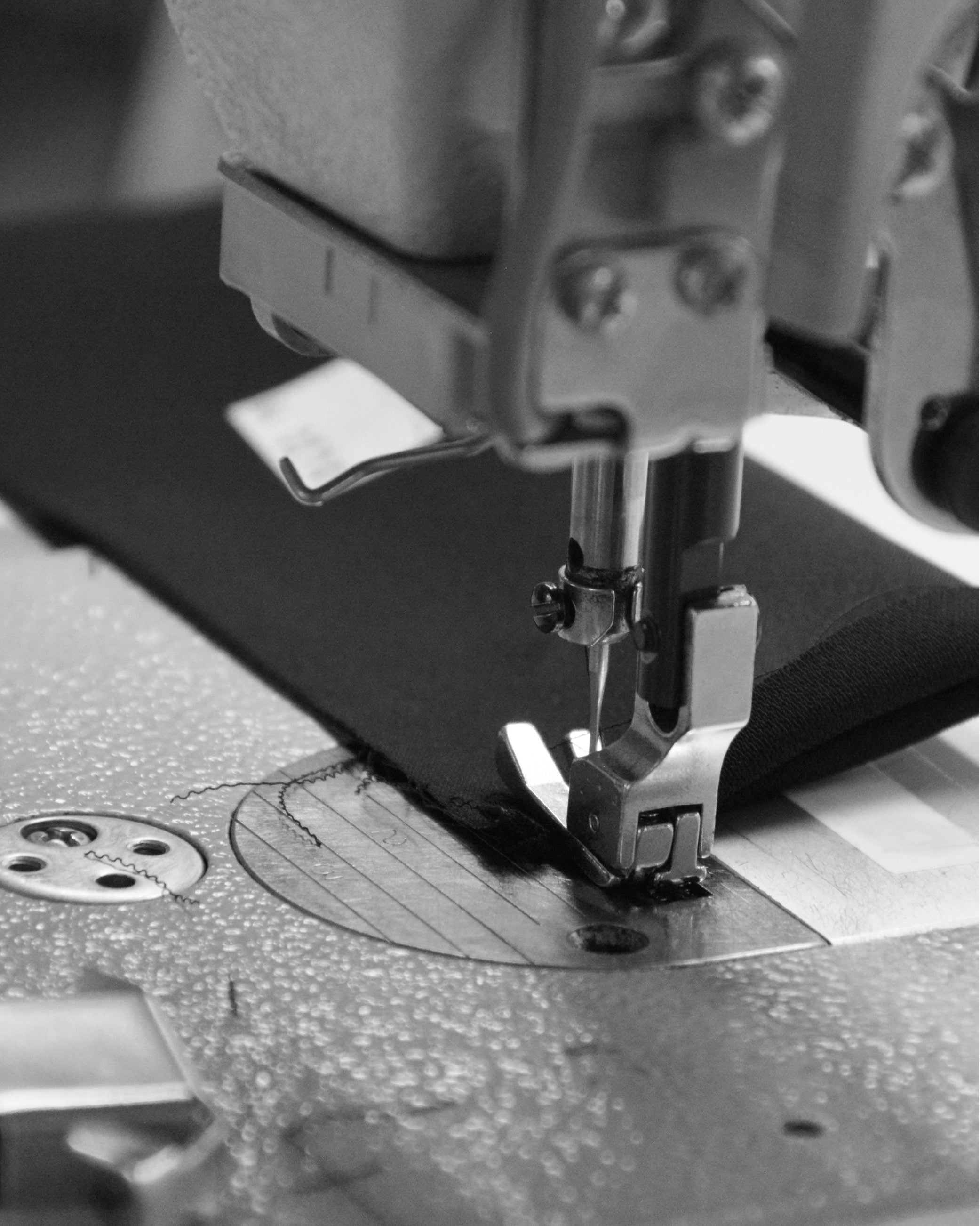 Close-up of a sewing machine needle stitching black fabric in black and white.
