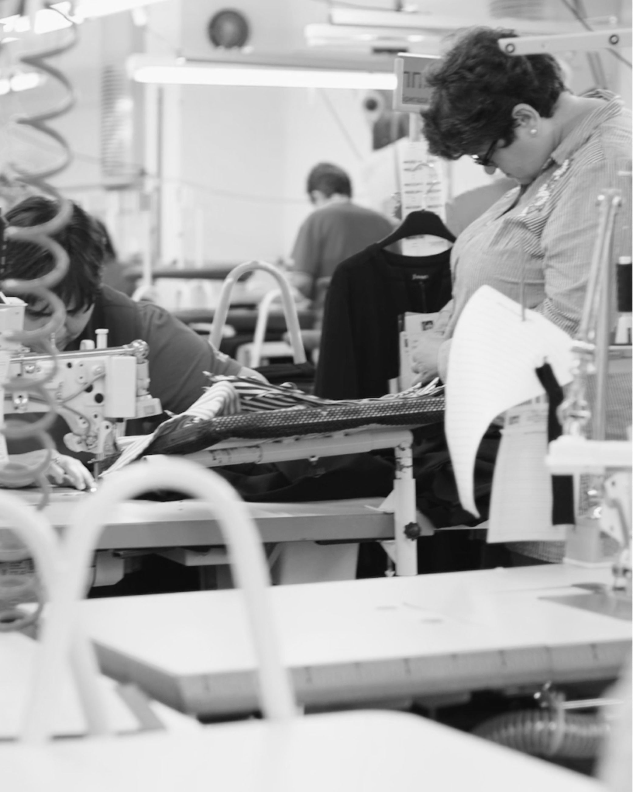 Two women working with sewing machines in a busy garment factory; clothing and tools are visible.
