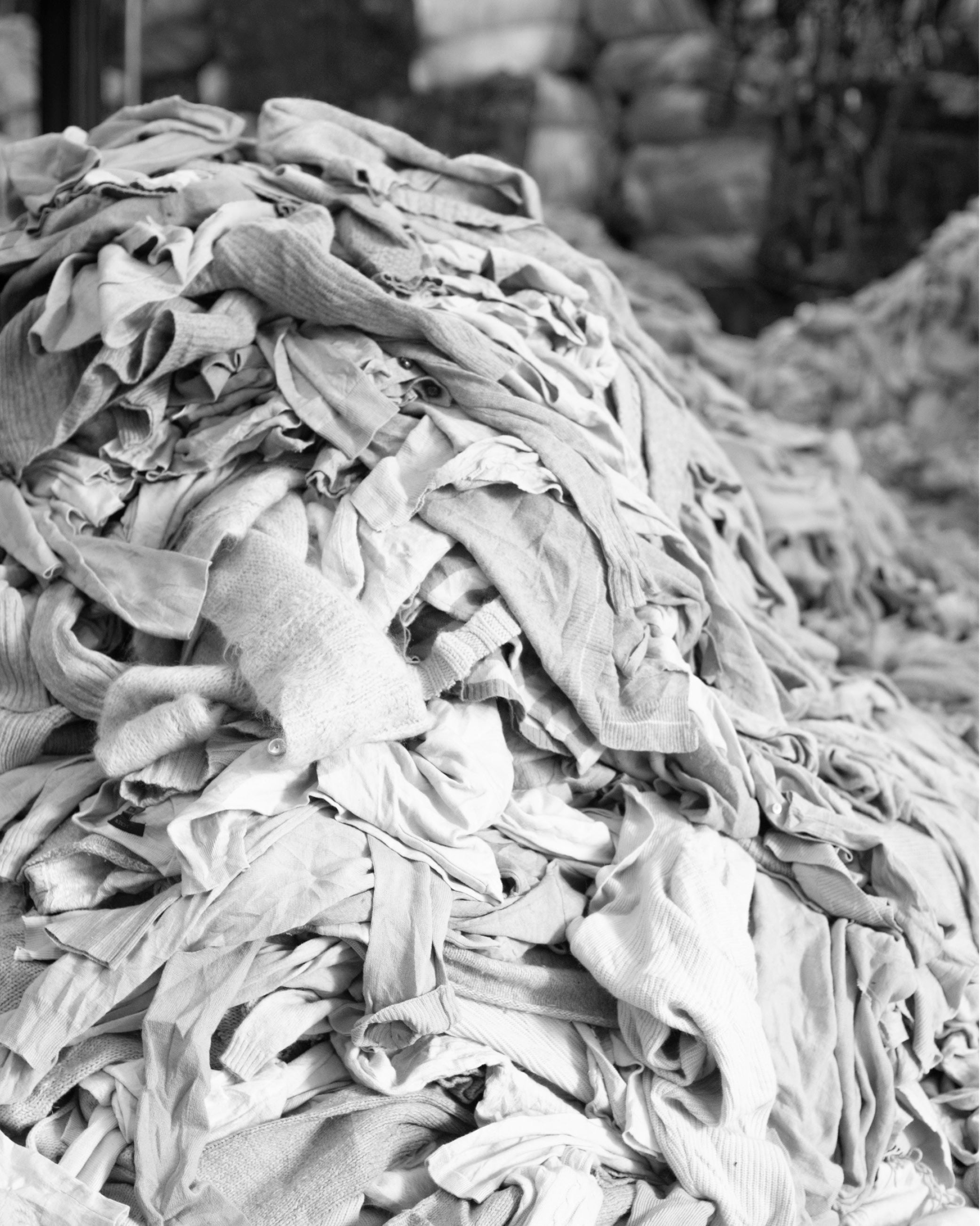 A large pile of old, crumpled clothes stacked together in black and white.