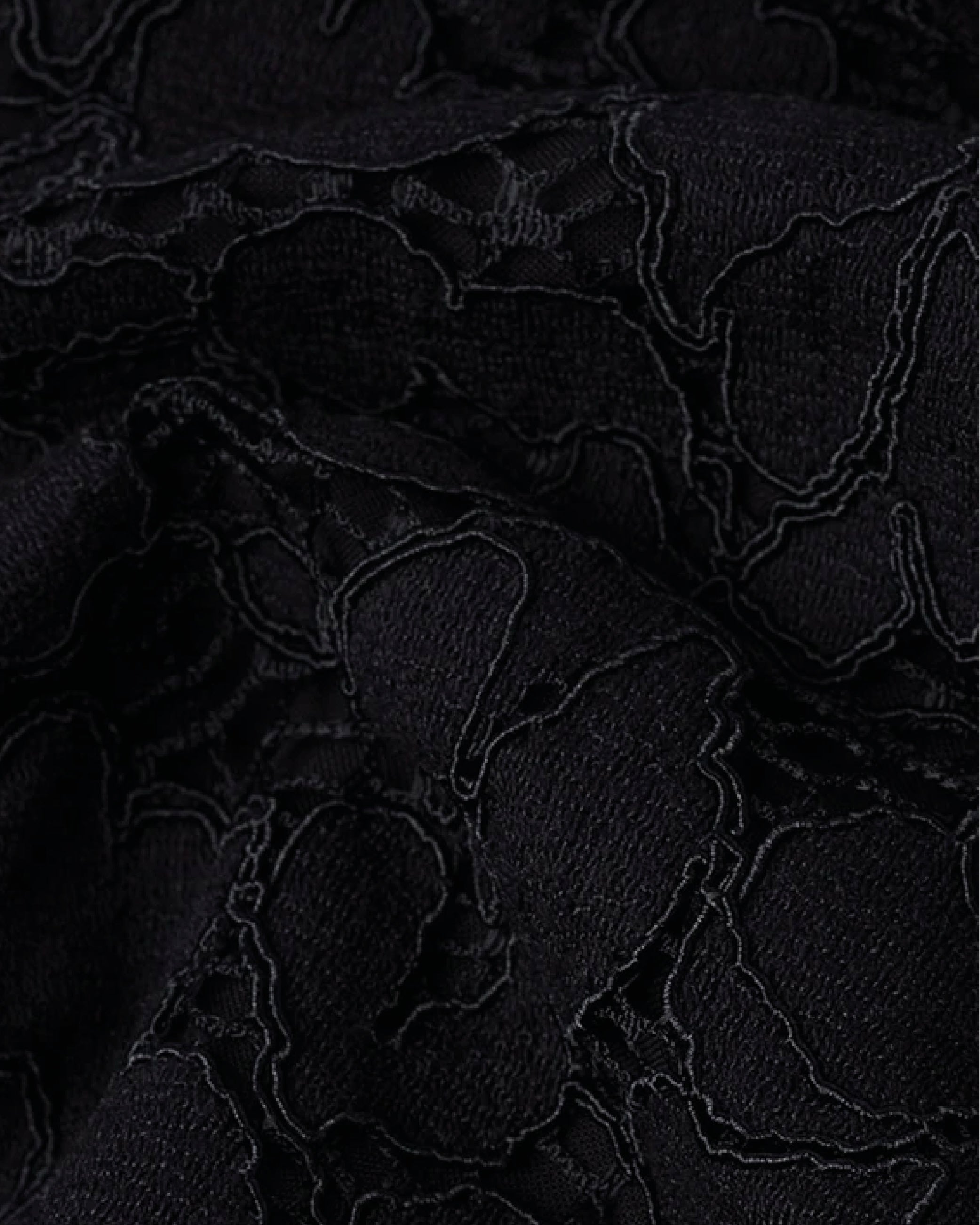 Close-up of black textured fabric with an embroidered floral lace pattern and slightly raised stitching.