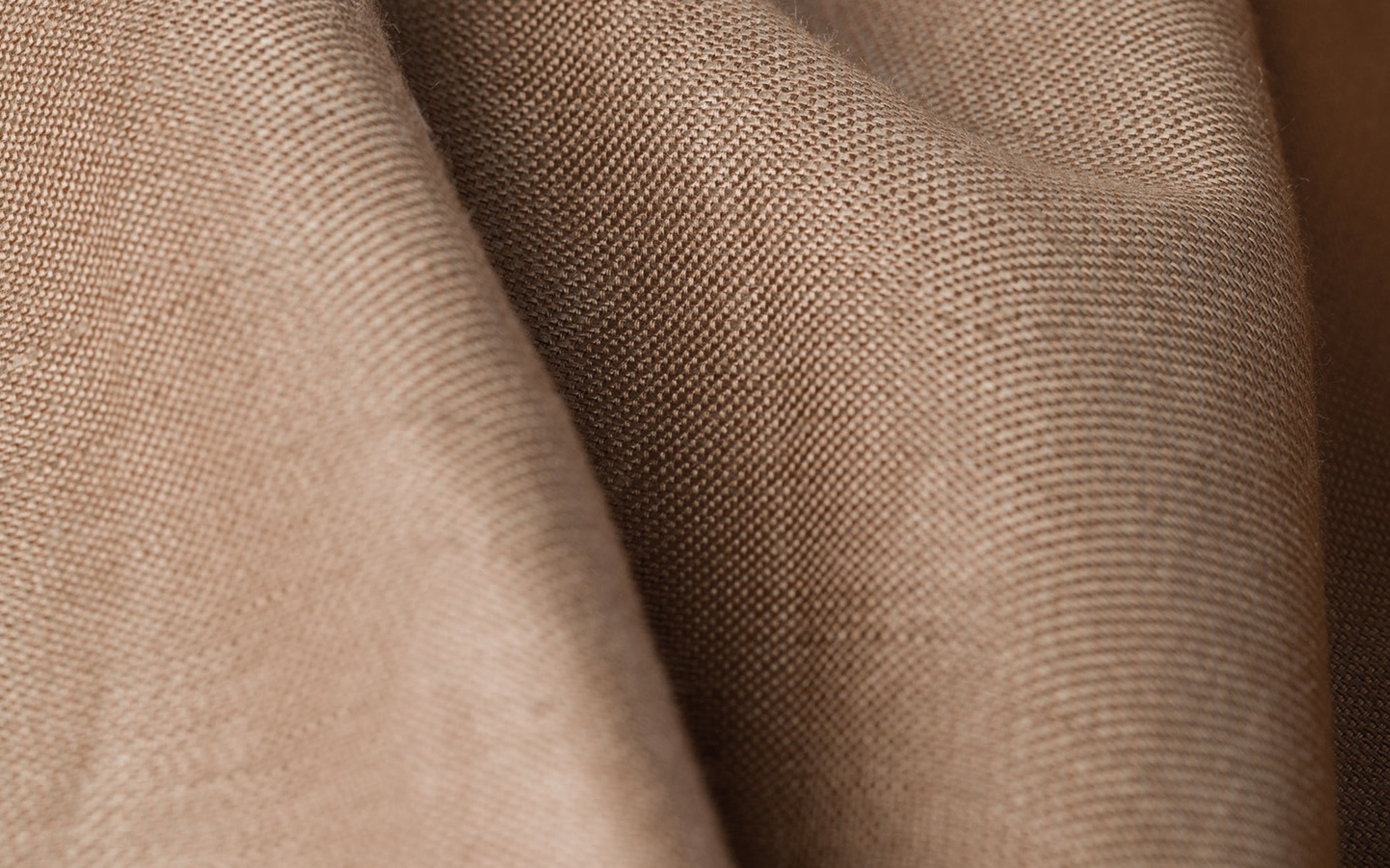 Close-up of light brown textured fabric with gentle folds and visible weave pattern.