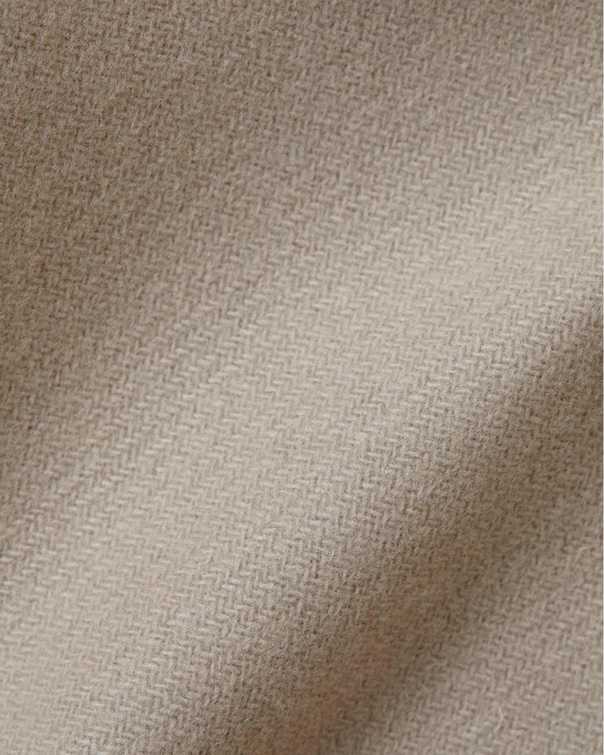 Close-up of beige herringbone patterned fabric with soft folds and textured woven surface.