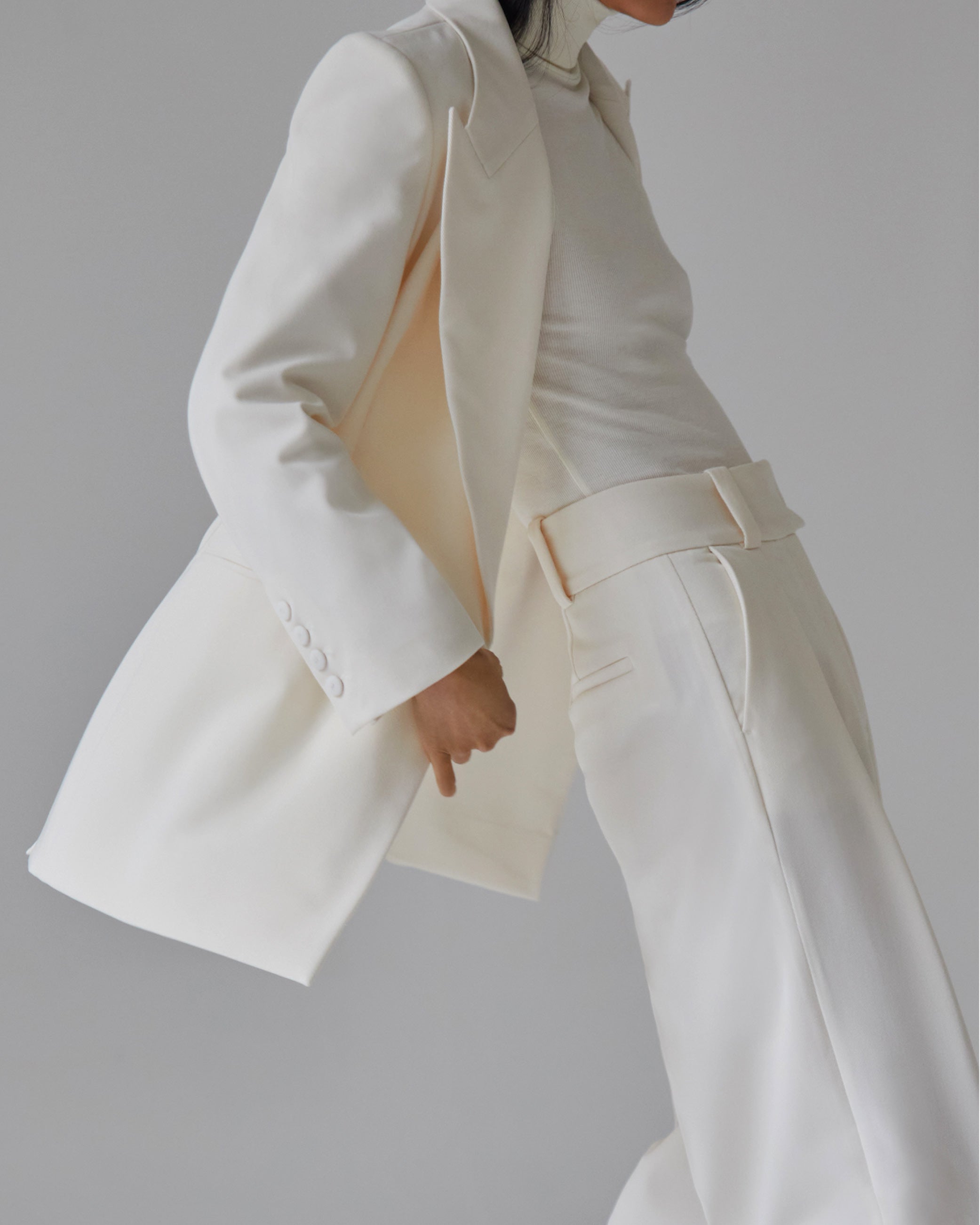 Person wearing an all-white suit with wide-leg pants and a fitted turtleneck, shown from the neck down.