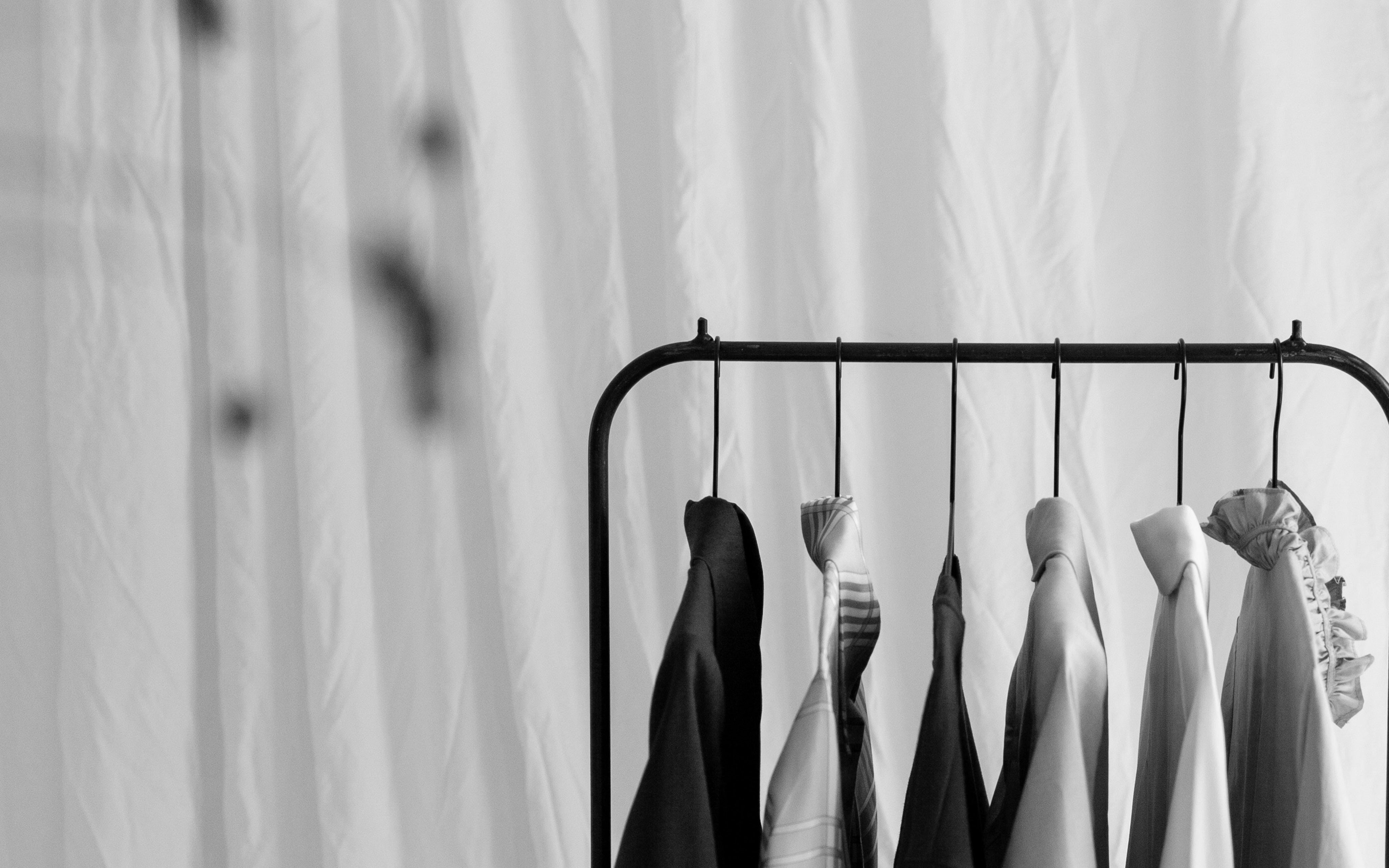 Black and white photo of various clothes hanging on a rack in front of a softly draped curtain.