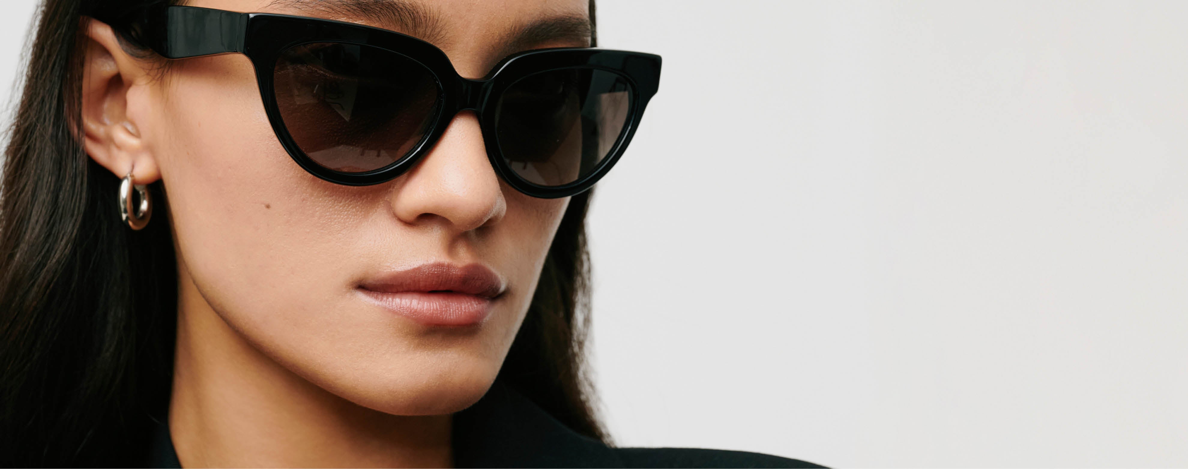 Woman wearing black cat-eye sunglasses and a hoop earring, with long dark hair and neutral expression.