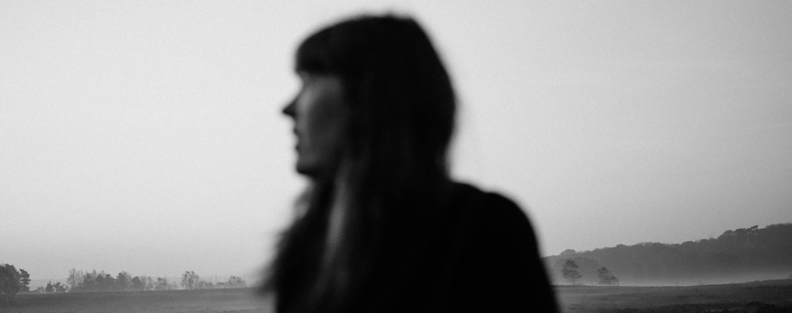 A blurry silhouette of a woman outdoors with a misty landscape in the background.
