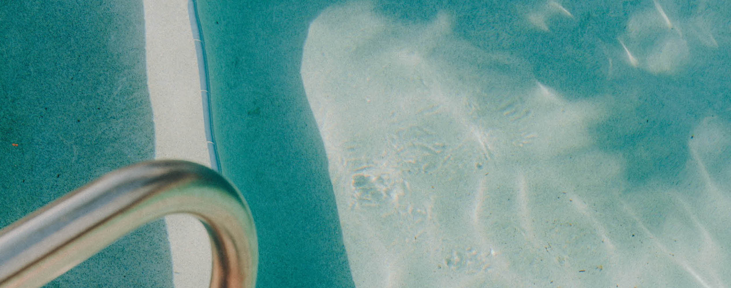 Close-up of a swimming pool corner with water ripples and a metal handrail on the left.