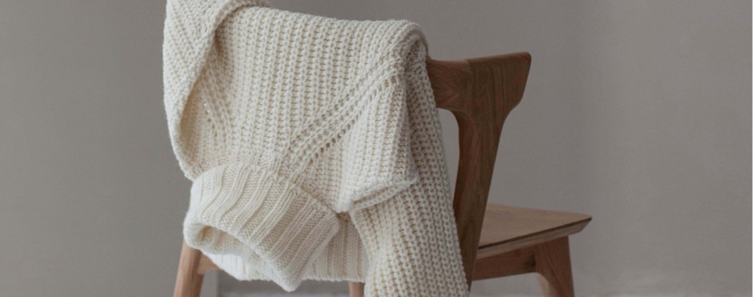 A cream-colored knitted sweater draped over the back of a wooden chair.