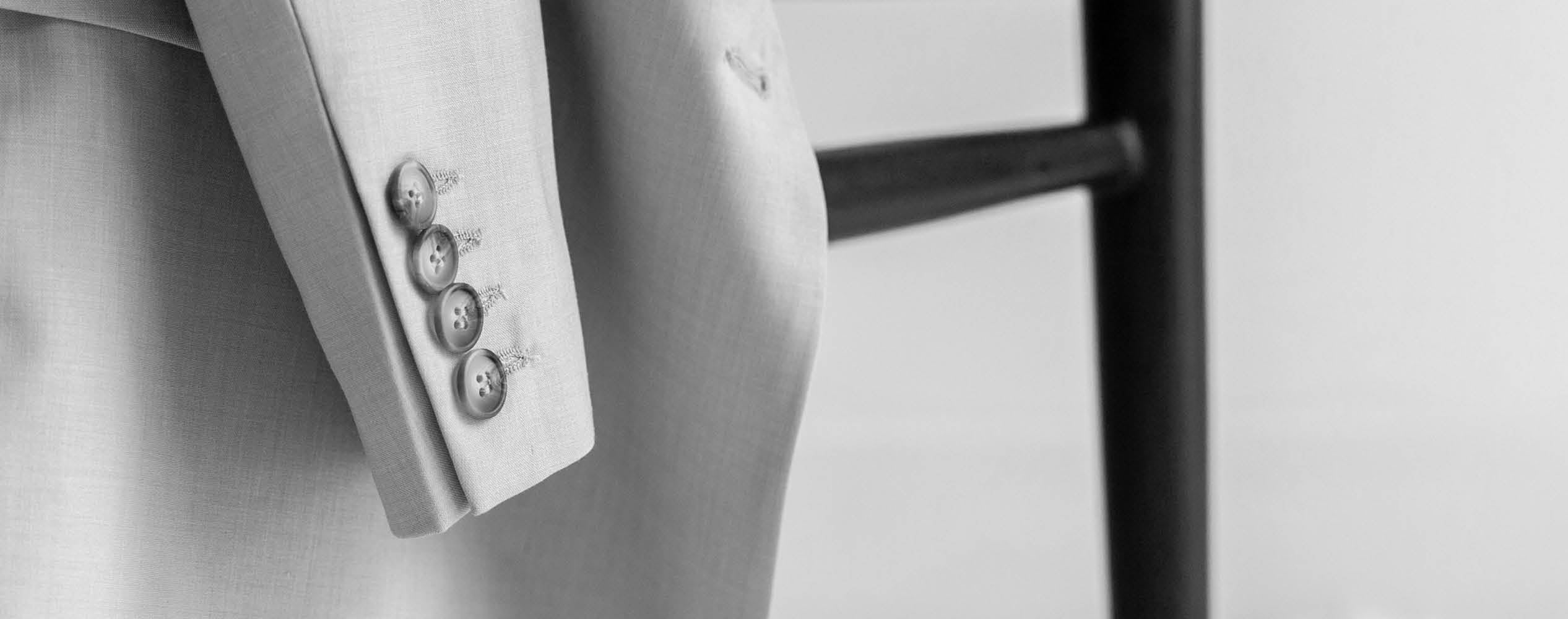Close-up of a light-colored suit sleeve with three buttons, next to the backrest of a dark wooden chair.