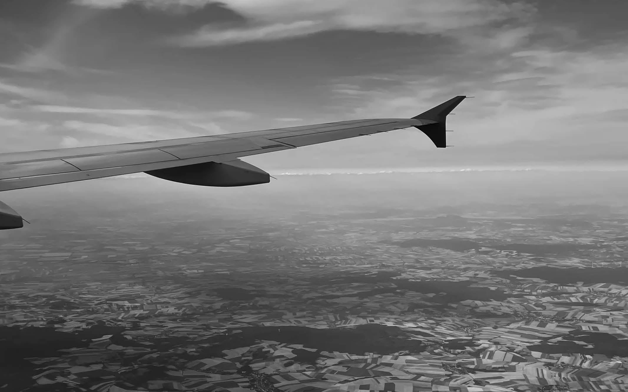 Aerial view of patchwork fields with an airplane wing visible under a partly cloudy sky.