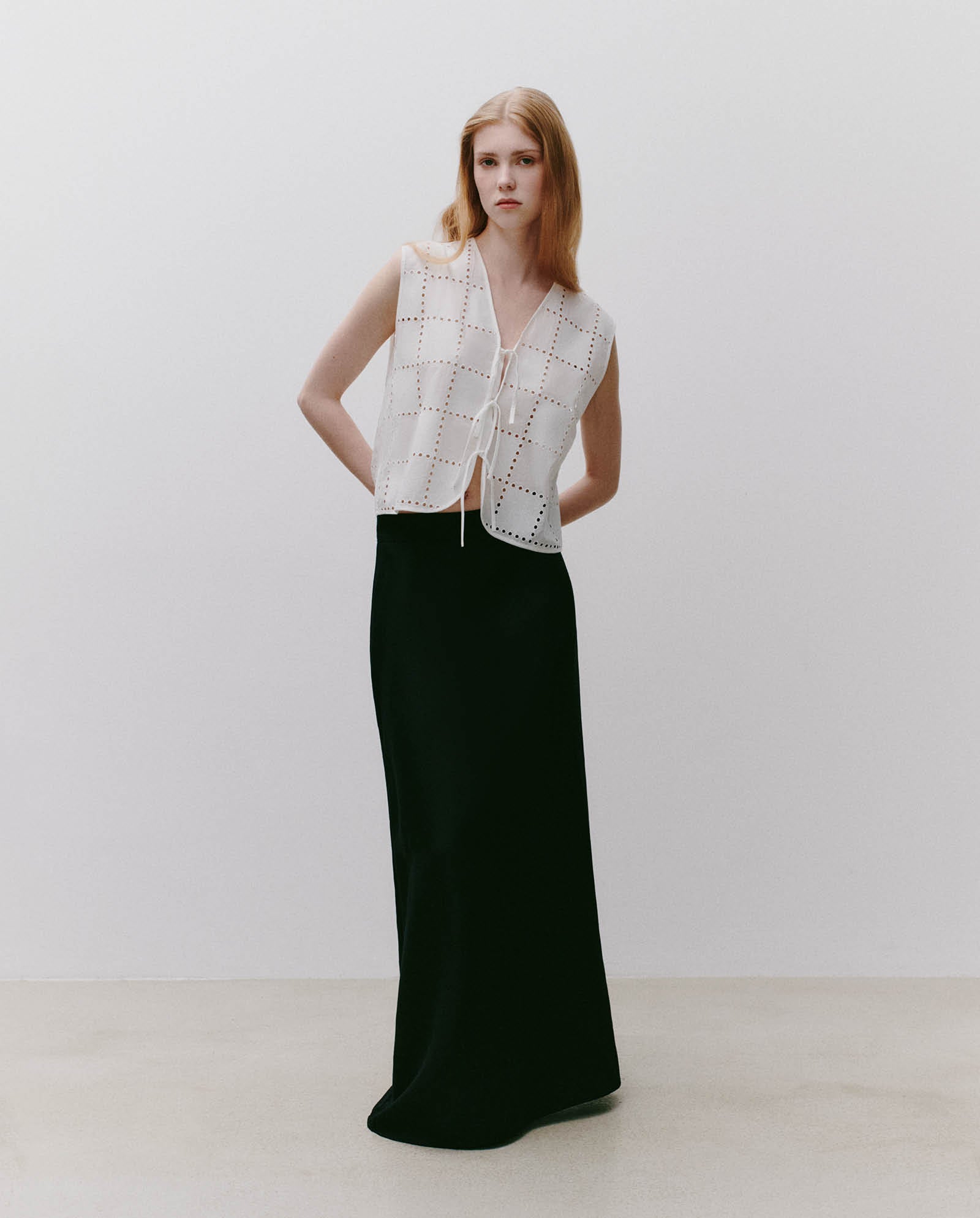A woman wears the IVY OAK TALA Top, featuring square cutouts and sleeveless design, paired with a long black skirt against a plain background.