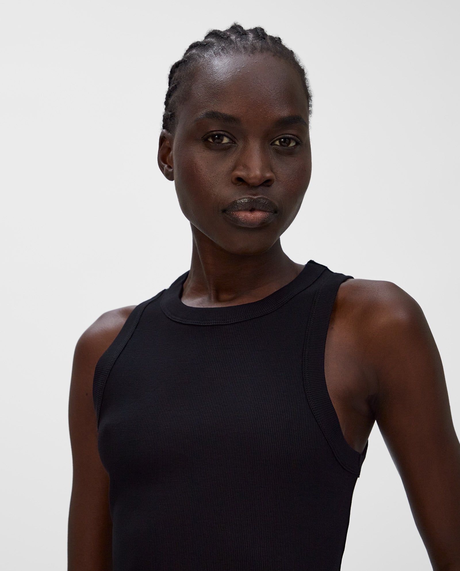 A woman with braided hair wears a sleeveless black KLARA ANN Tanktop by IVY OAK, made from organic cotton, standing against a plain white background.