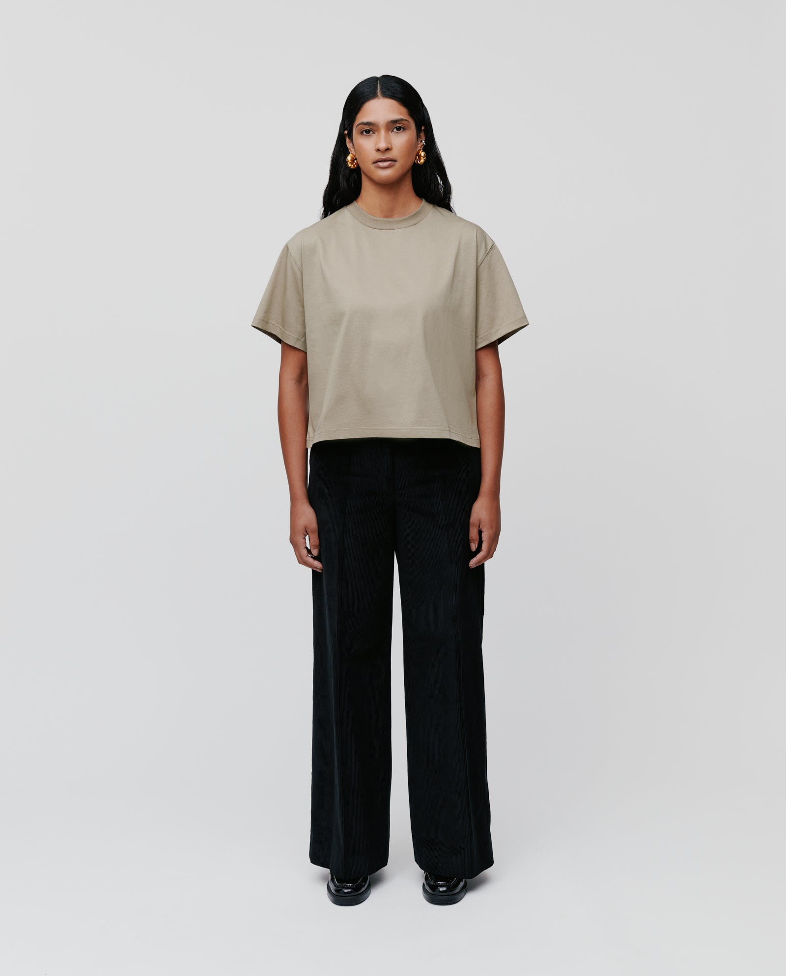 A woman wearing the IVY OAK KYLA Top, crafted from organic cotton, styled with black wide-leg pants and black shoes against a plain background.
