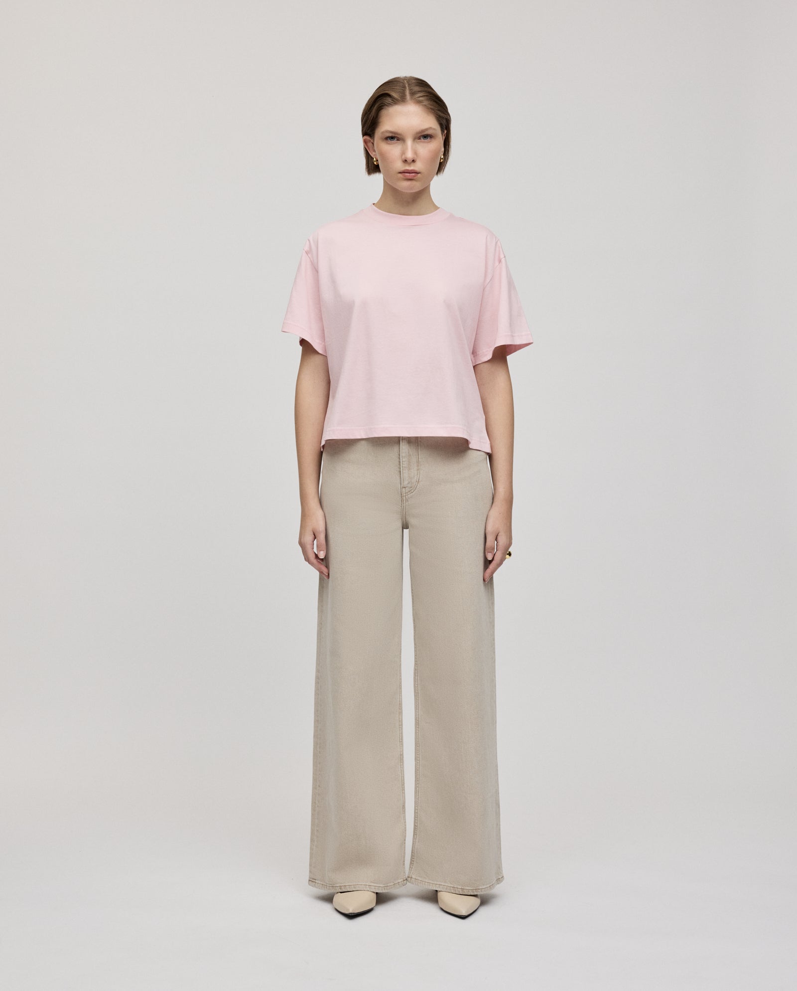 A woman stands facing forward in a pink IVY OAK KYLA Top made from organic cotton and beige wide-leg pants against a plain background—a basic must-have look.