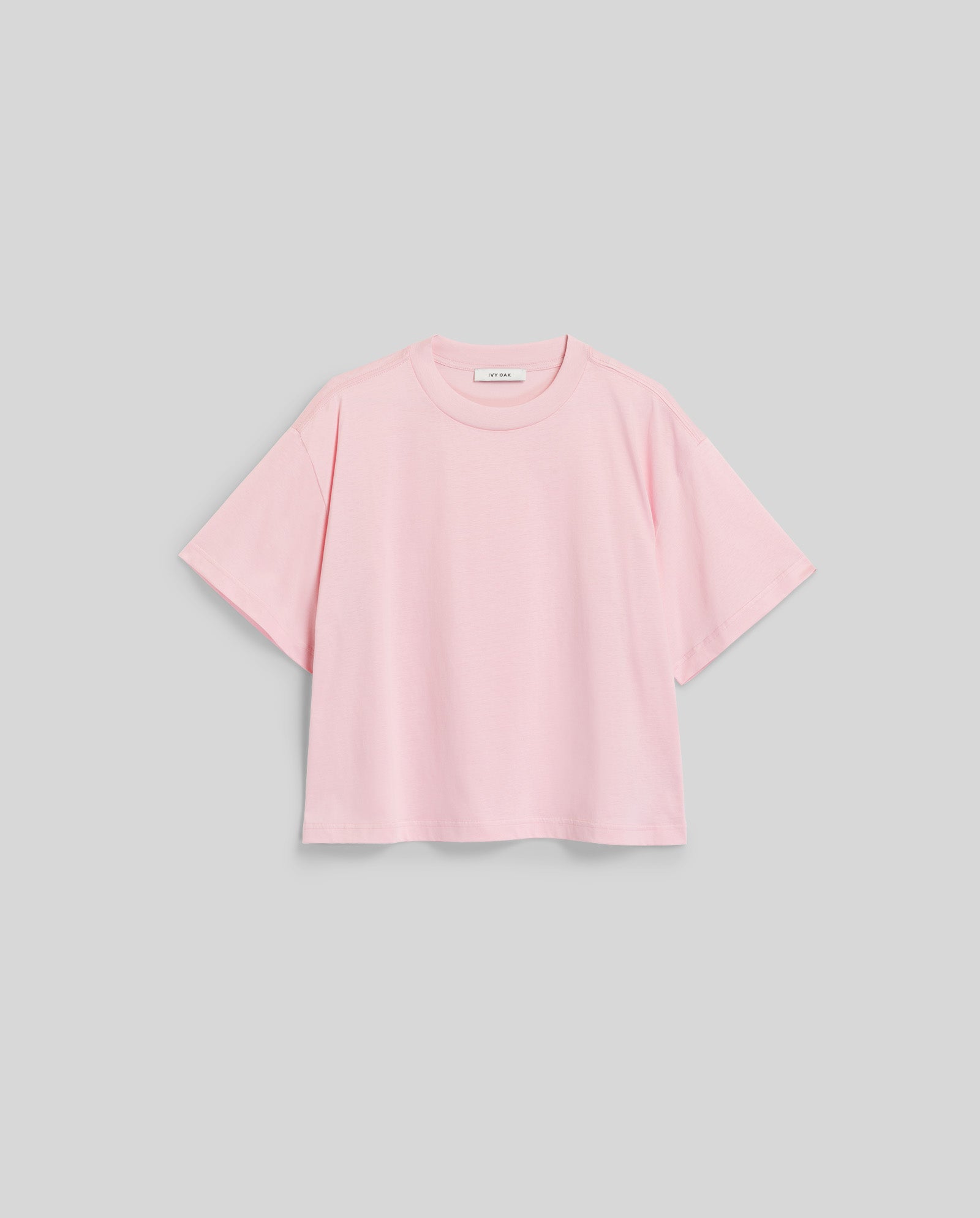 The IVY OAK KYLA Top is a light pink, organic cotton short-sleeve essential, shown on a plain gray background—a basic must-have for any wardrobe.