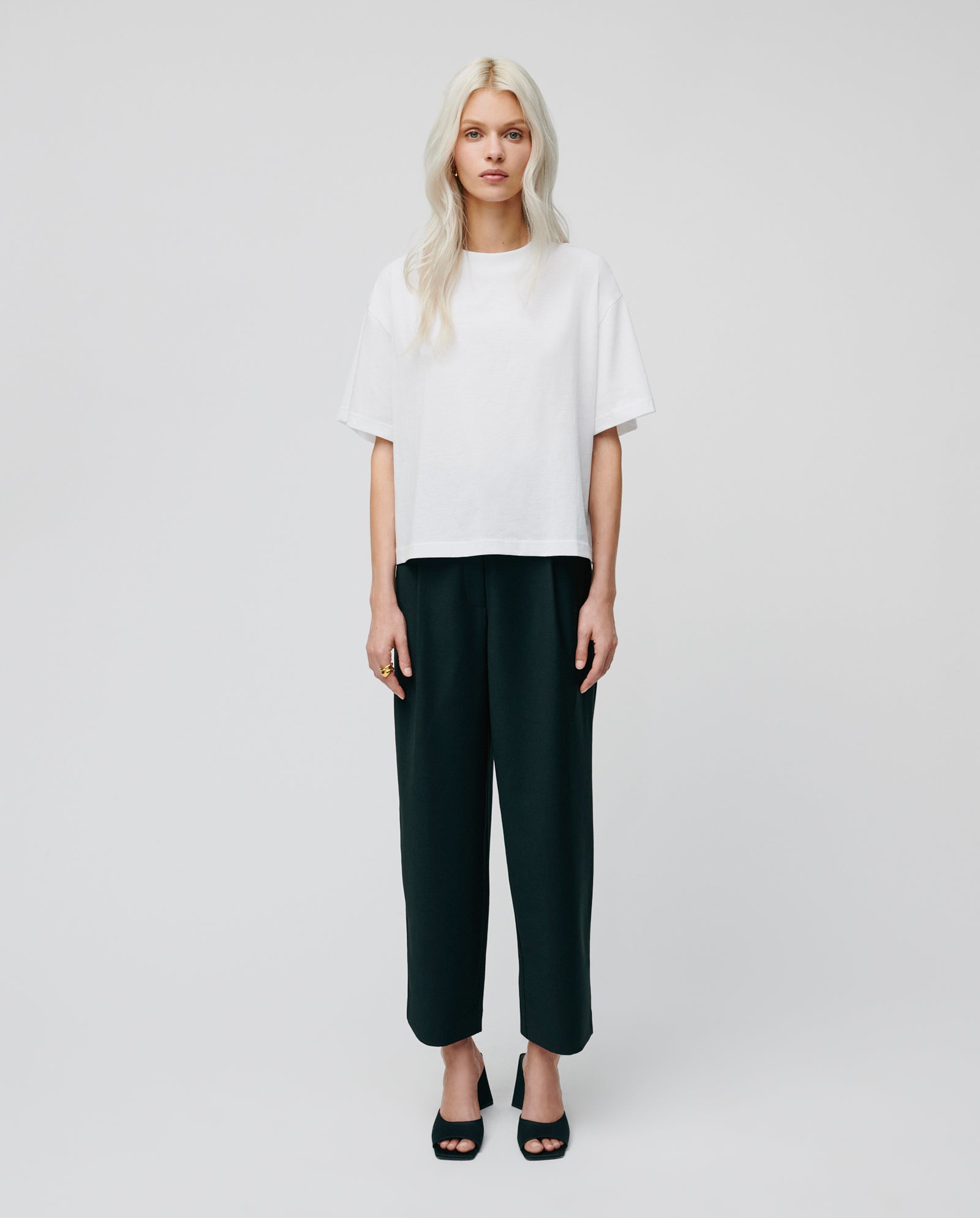 Woman with long blonde hair wears the must-have KYLA Top by IVY OAK in organic cotton, paired with black pants against a plain background.