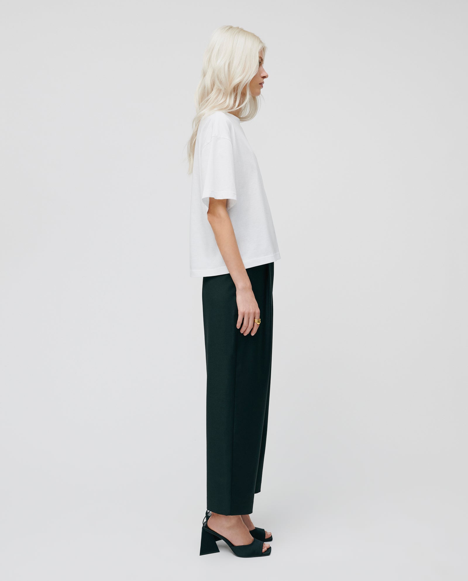 A woman with long blonde hair wears the IVY OAK KYLA Top, made from organic cotton, paired with black pants and black heels, standing in profile.