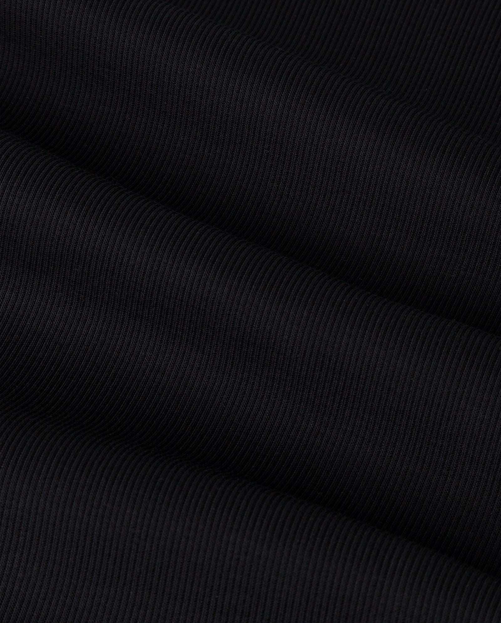 Close-up of comfortable black ribbed fabric with diagonal folds creating subtle shadows and texture, featured in the KOLLINA Top by IVY OAK.