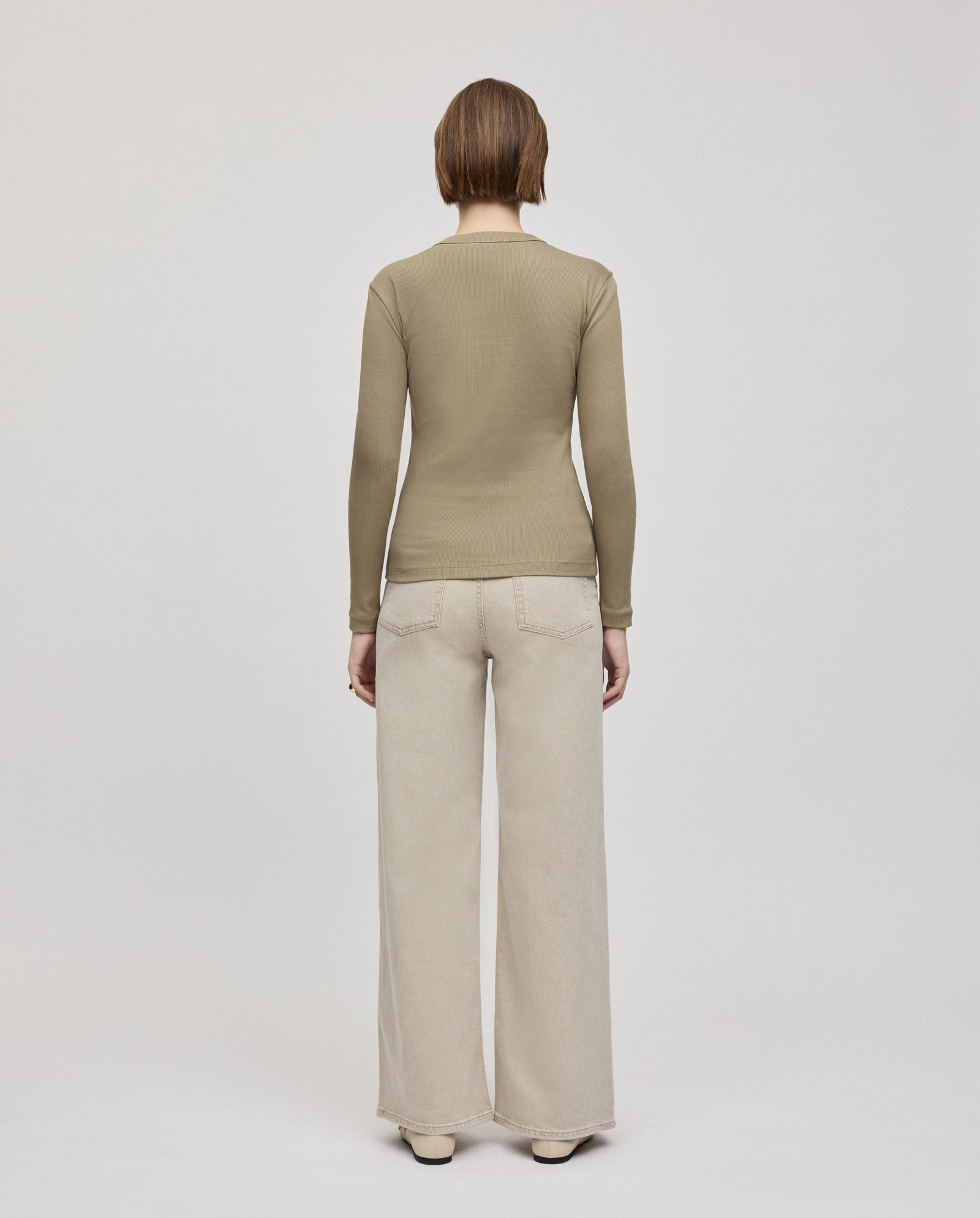 A person stands with their back to the camera, wearing the IVY OAK KOLLINA Top made from organic cotton, paired with wide-leg beige pants.