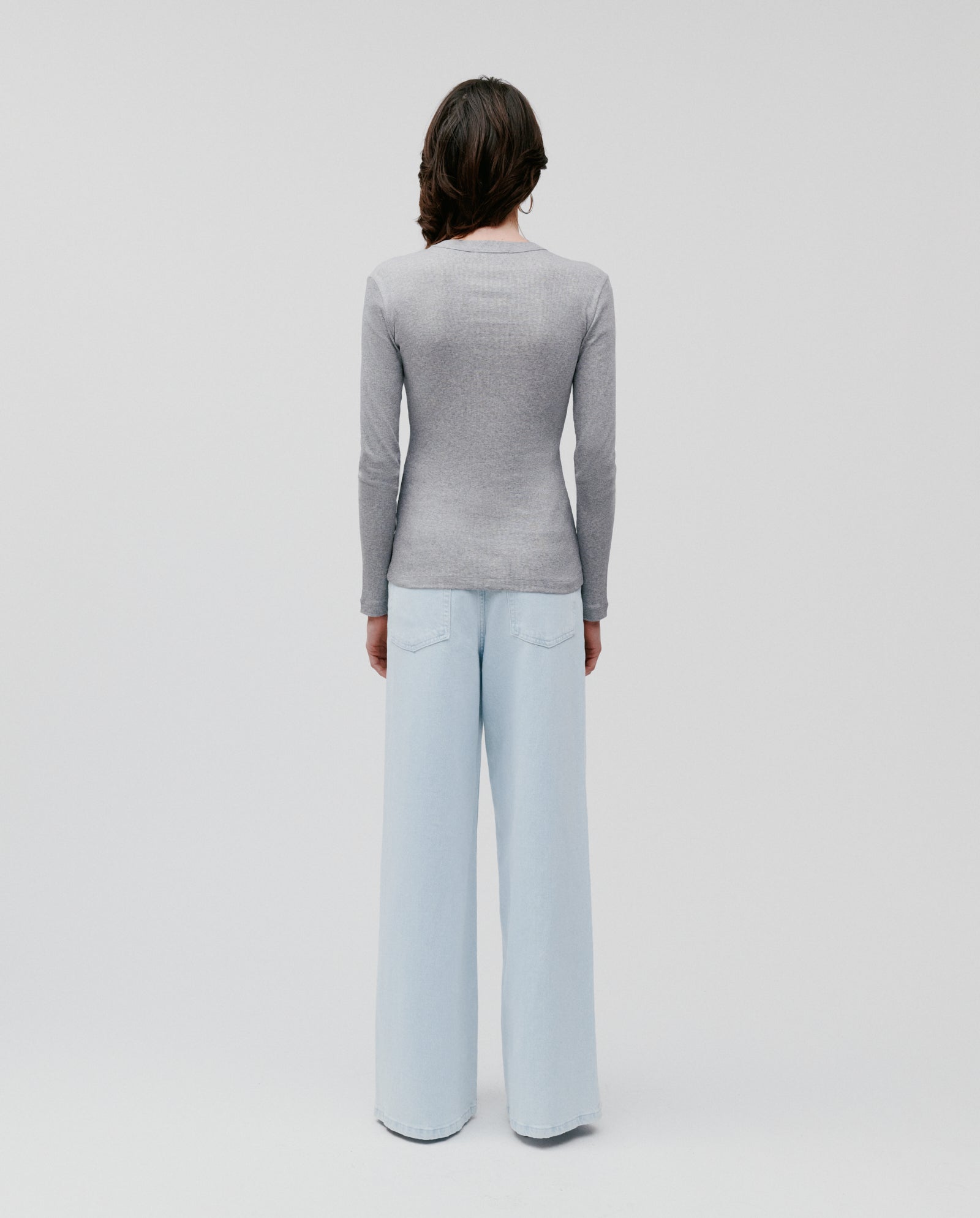 Person stands with back to camera, wearing the IVY OAK KOLLINA Top in grey organic cotton with a round neck and light blue wide-leg jeans.