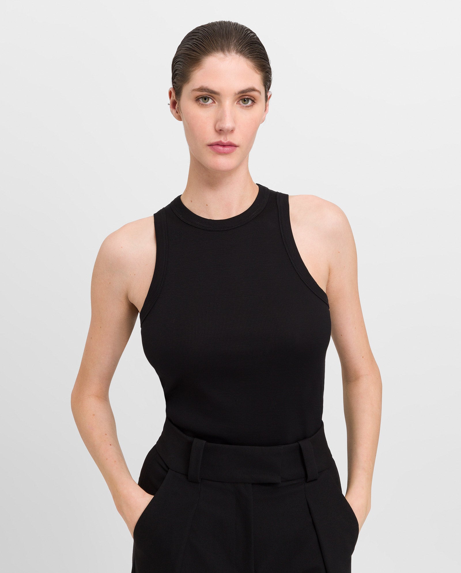 KLARA ANN, a woman with brown hair in a sleek bun, stands confidently wearing the black KLARA ANN Top by IVY OAK paired with matching black pants.