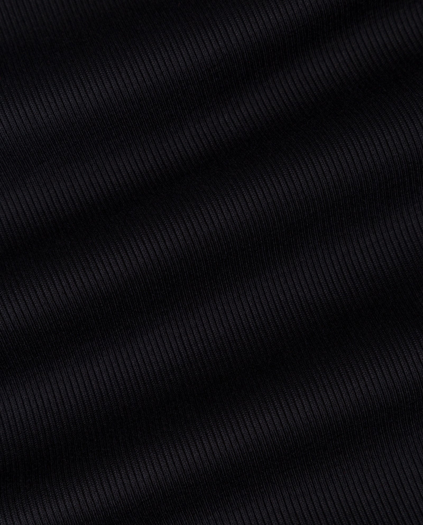 Close-up of IVY OAK’s KLARA ANN Top in black ribbed fabric featuring diagonal textured lines and subtle shadows, crafted from soft organic cotton—ideal for a tank top.