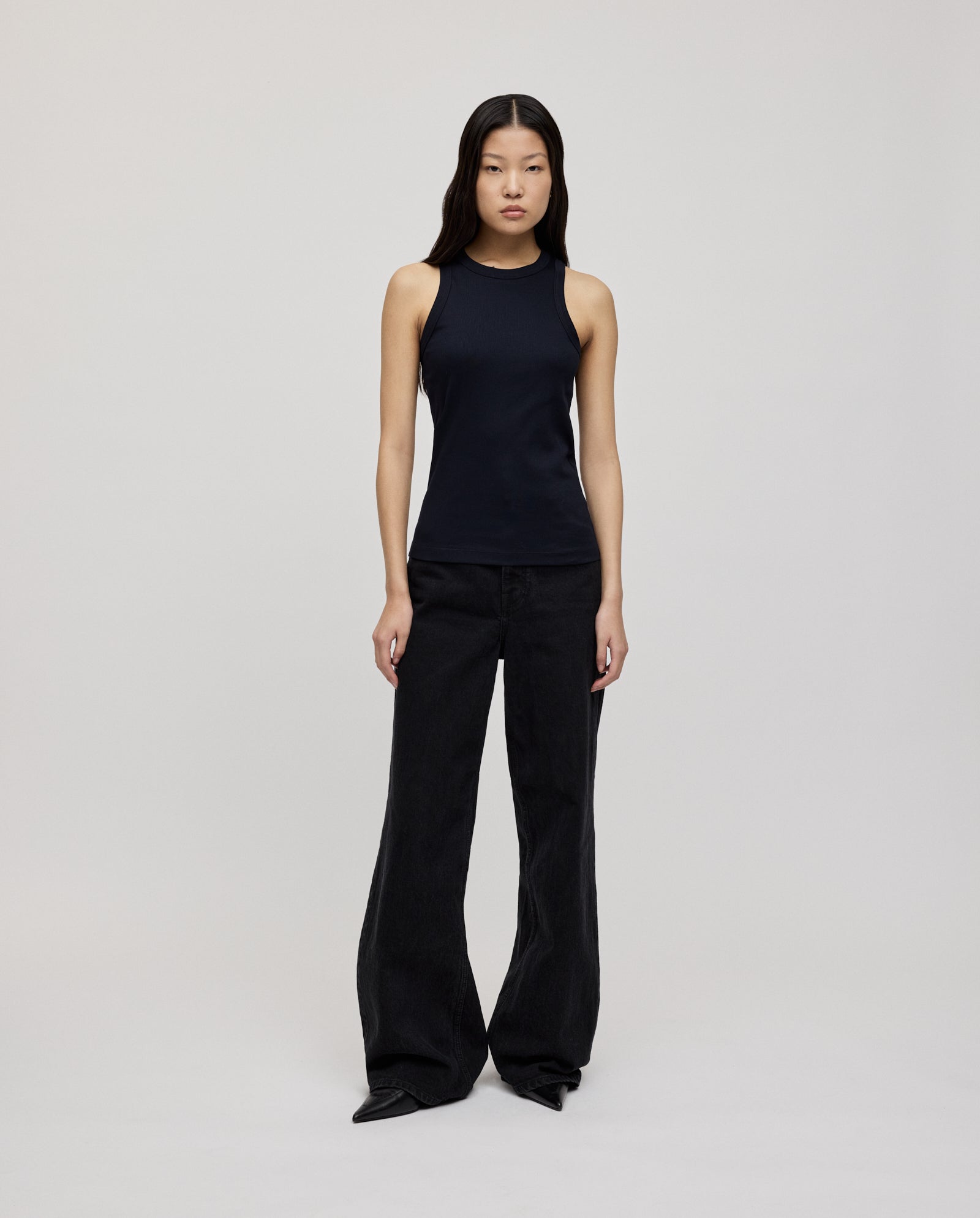 A woman wears the KLARA ANN Top by IVY OAK, a comfortable black tank made from soft organic cotton, paired with wide-leg black pants, standing against a plain light background.