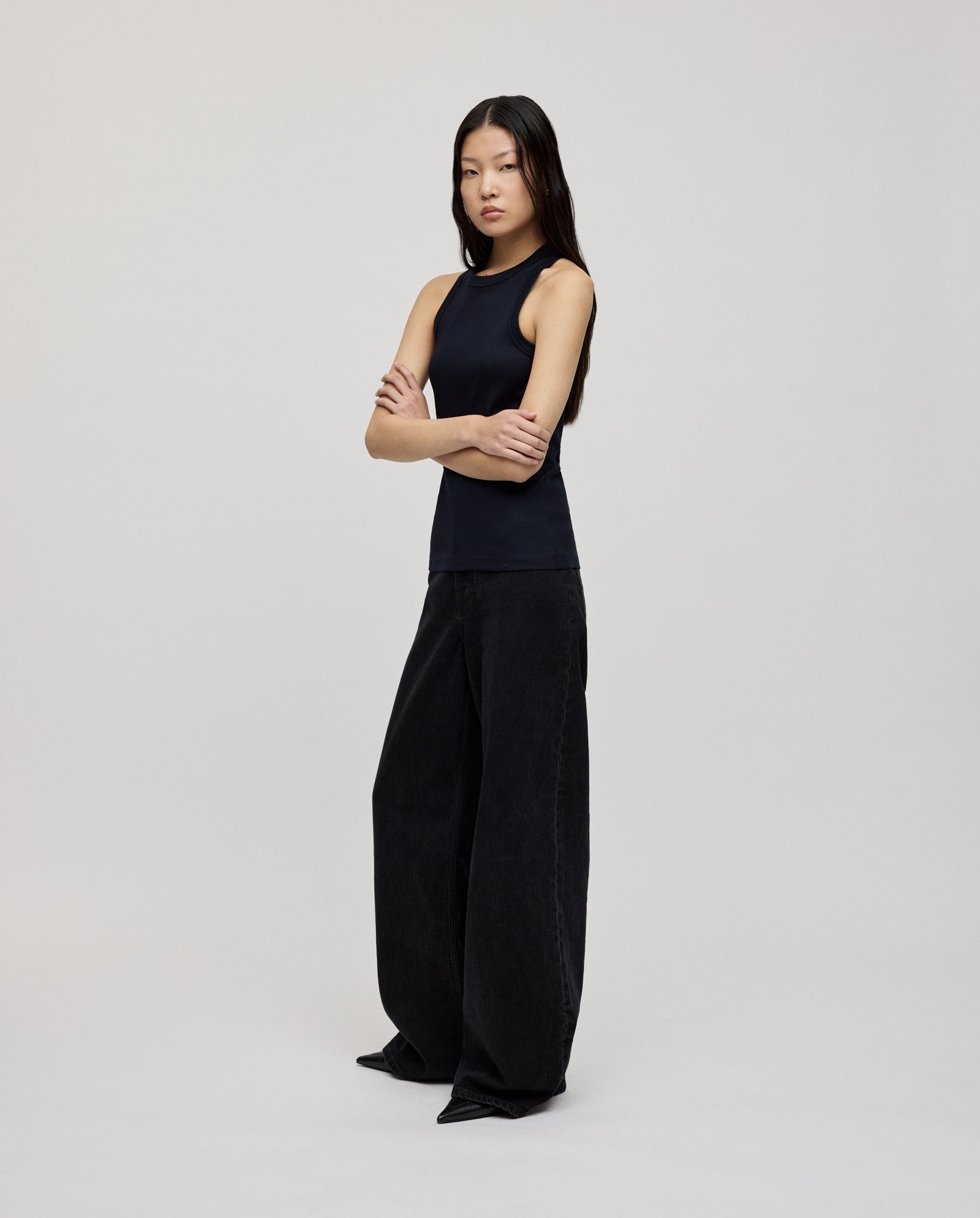 A woman stands with arms crossed against a plain background, wearing the KLARA ANN Top by IVY OAK—an organic cotton tank paired with wide-leg pants for a comfortable, effortless look.
