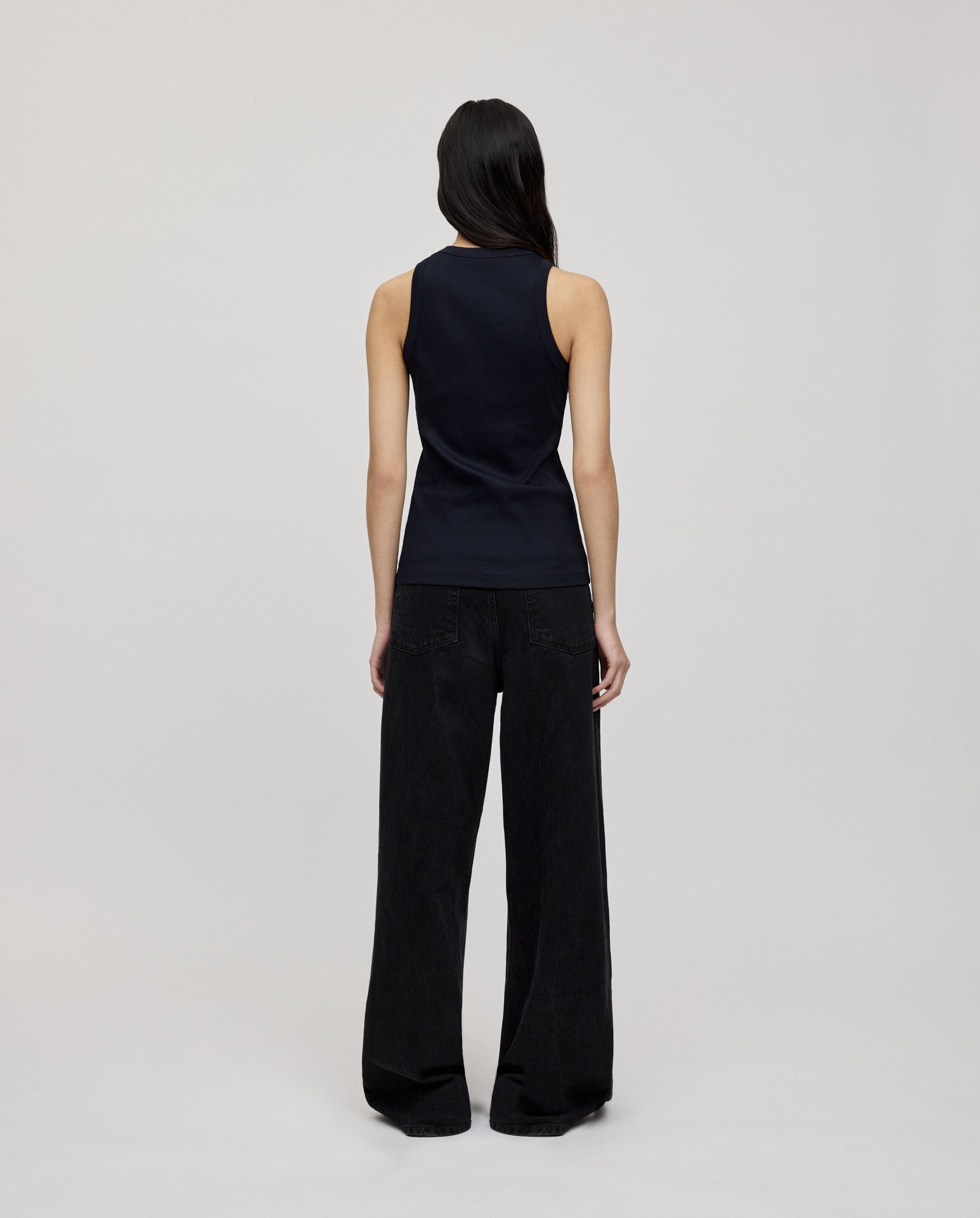 A person faces away, wearing the IVY OAK KLARA ANN Top in black organic cotton with wide-leg black pants, set against a plain background.