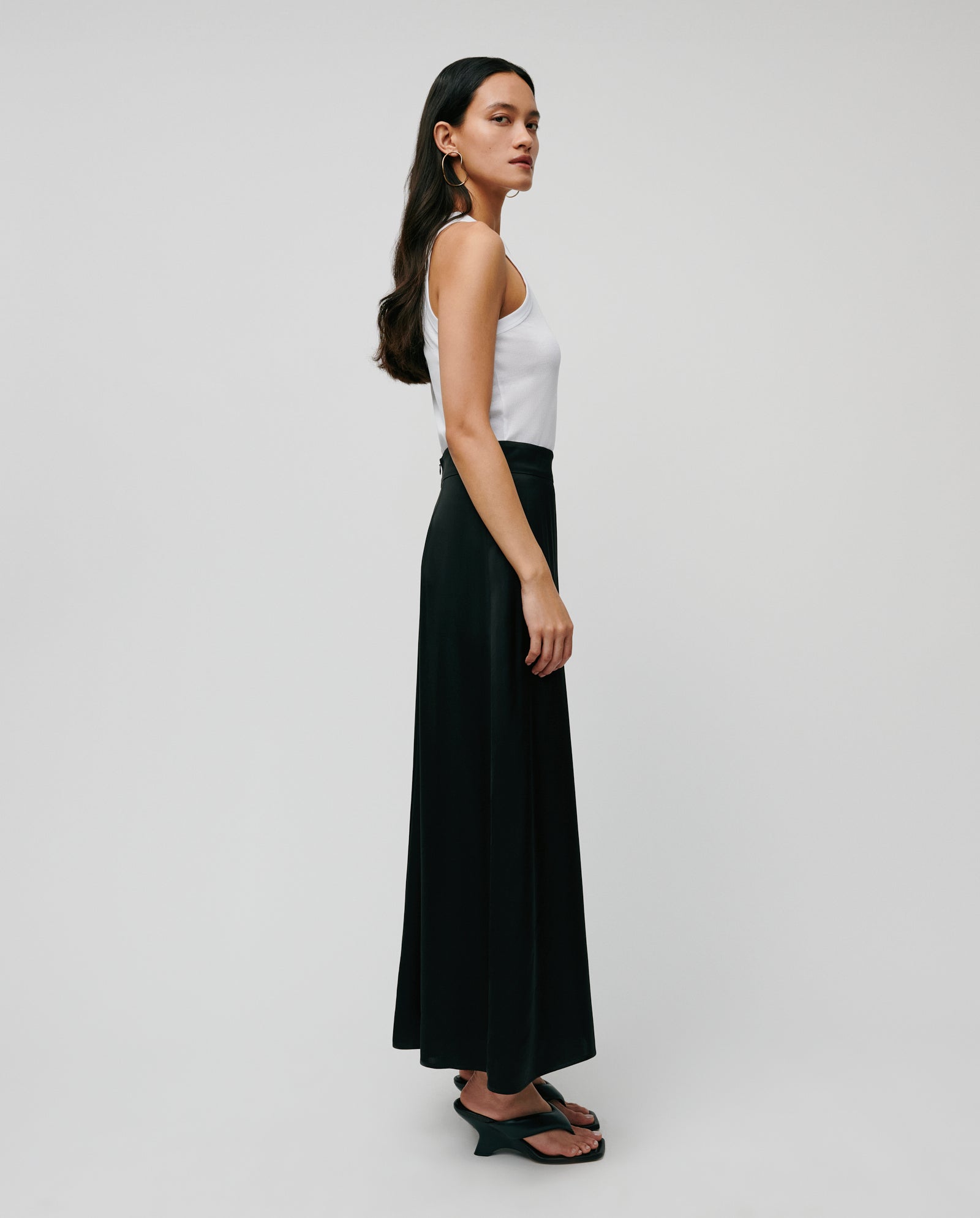 KLARA ANN models the IVY OAK KLARA ANN Top in white organic cotton, paired with a black skirt, standing in profile against a plain light backdrop.