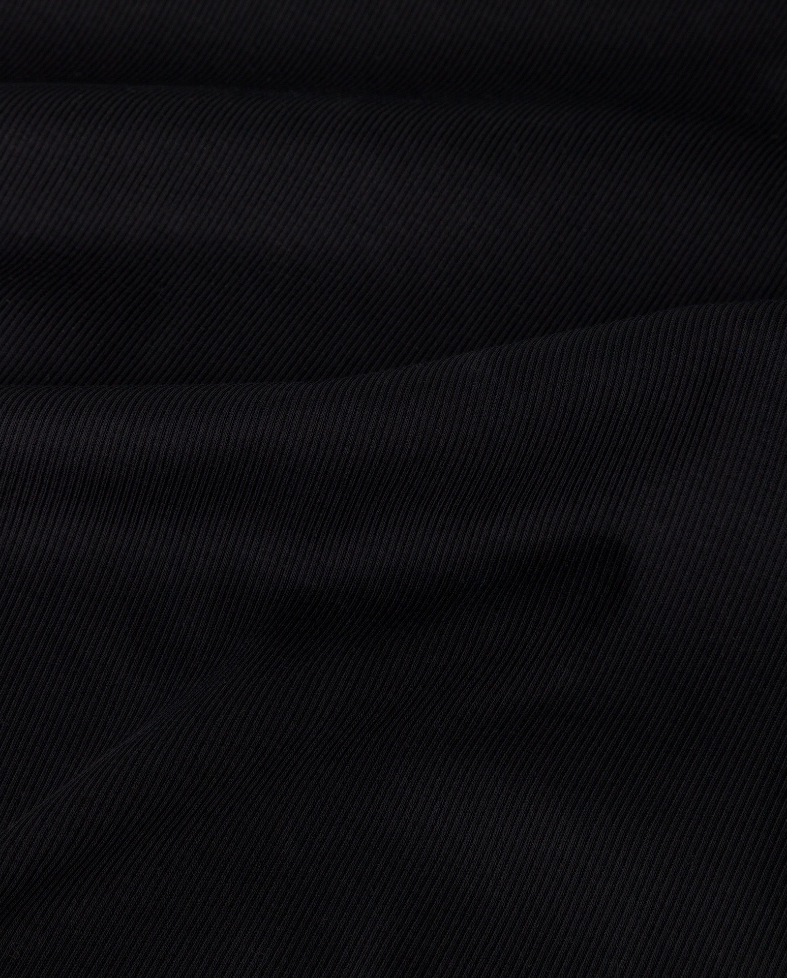 Close-up of black ribbed fabric with diagonal textured lines and soft folds, highlighting the comfortable organic cotton feel of the KRISTIN Top from IVY OAK.