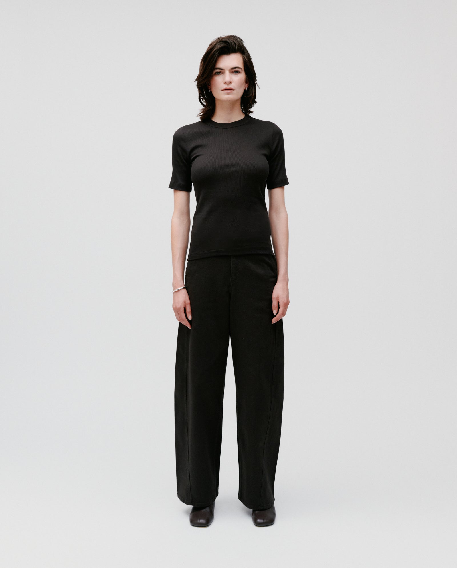 A person faces forward, wearing the IVY OAK KRISTIN Top made from organic cotton and wide-leg black pants against a plain background.