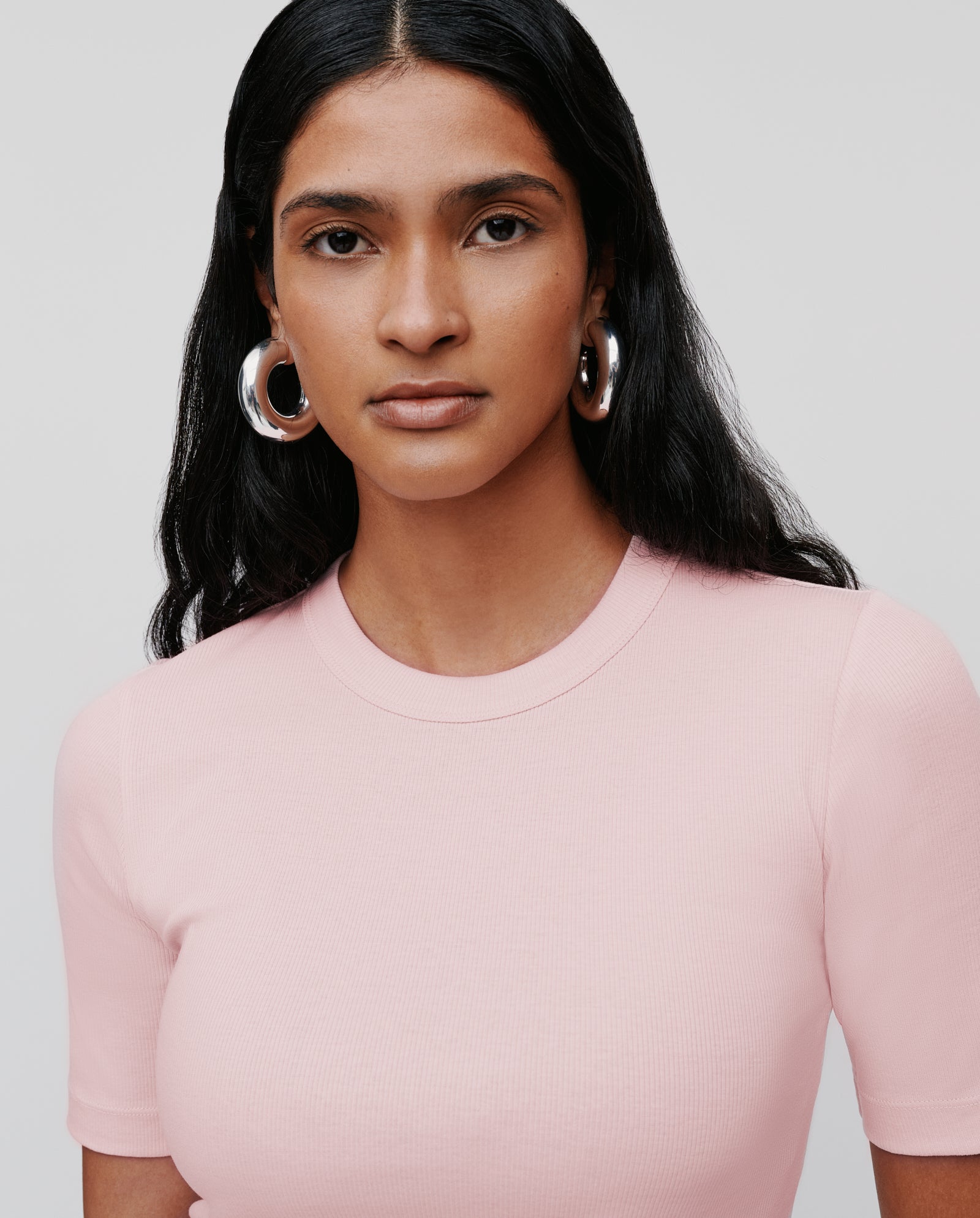 Woman with long black hair wears a light pink, comfortable IVY OAK KRISTIN Top made from organic cotton and large silver hoop earrings, facing forward.