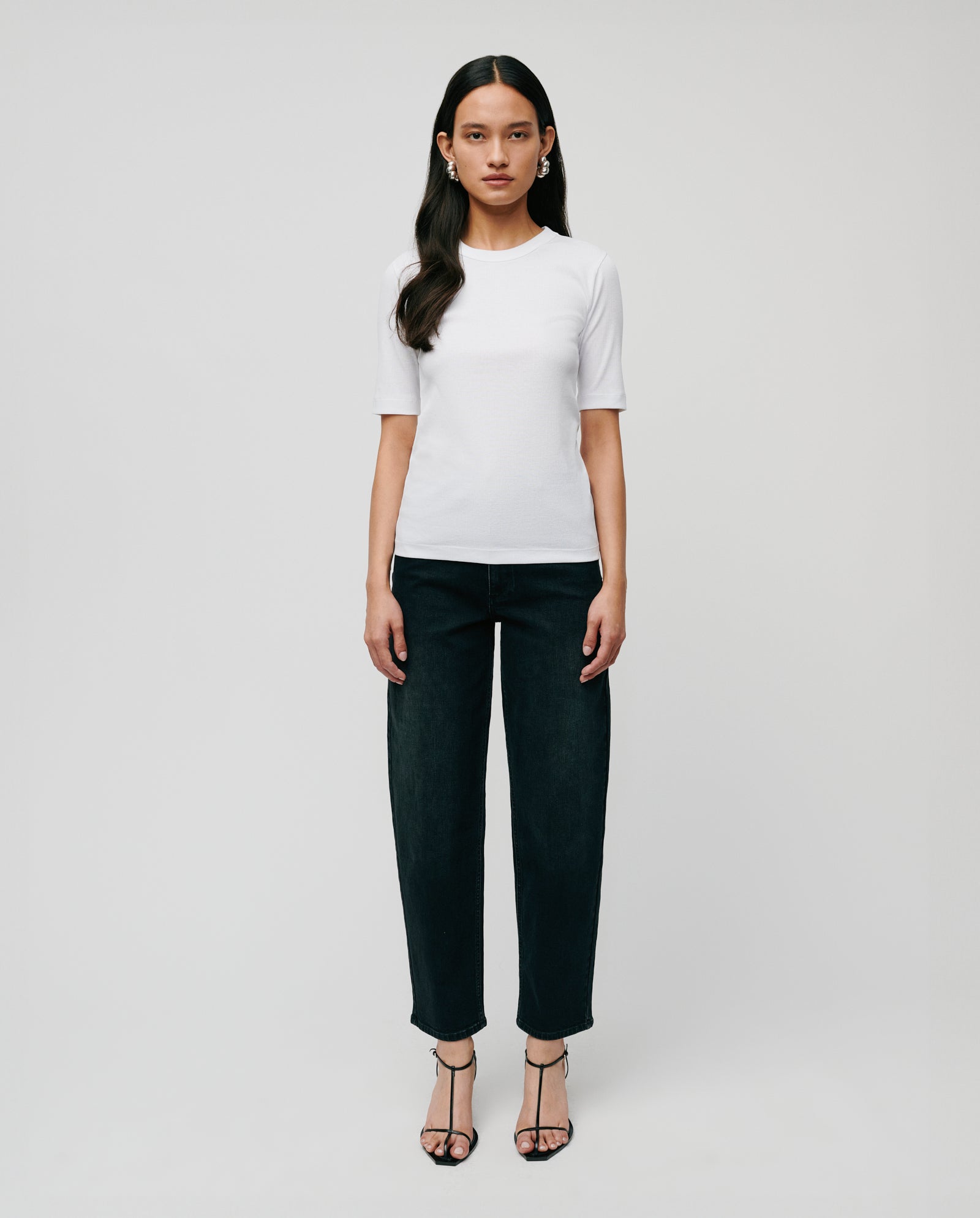 A woman faces forward in a comfortable IVY OAK KRISTIN Top made from organic cotton, styled with dark jeans and black heeled sandals against a plain background.