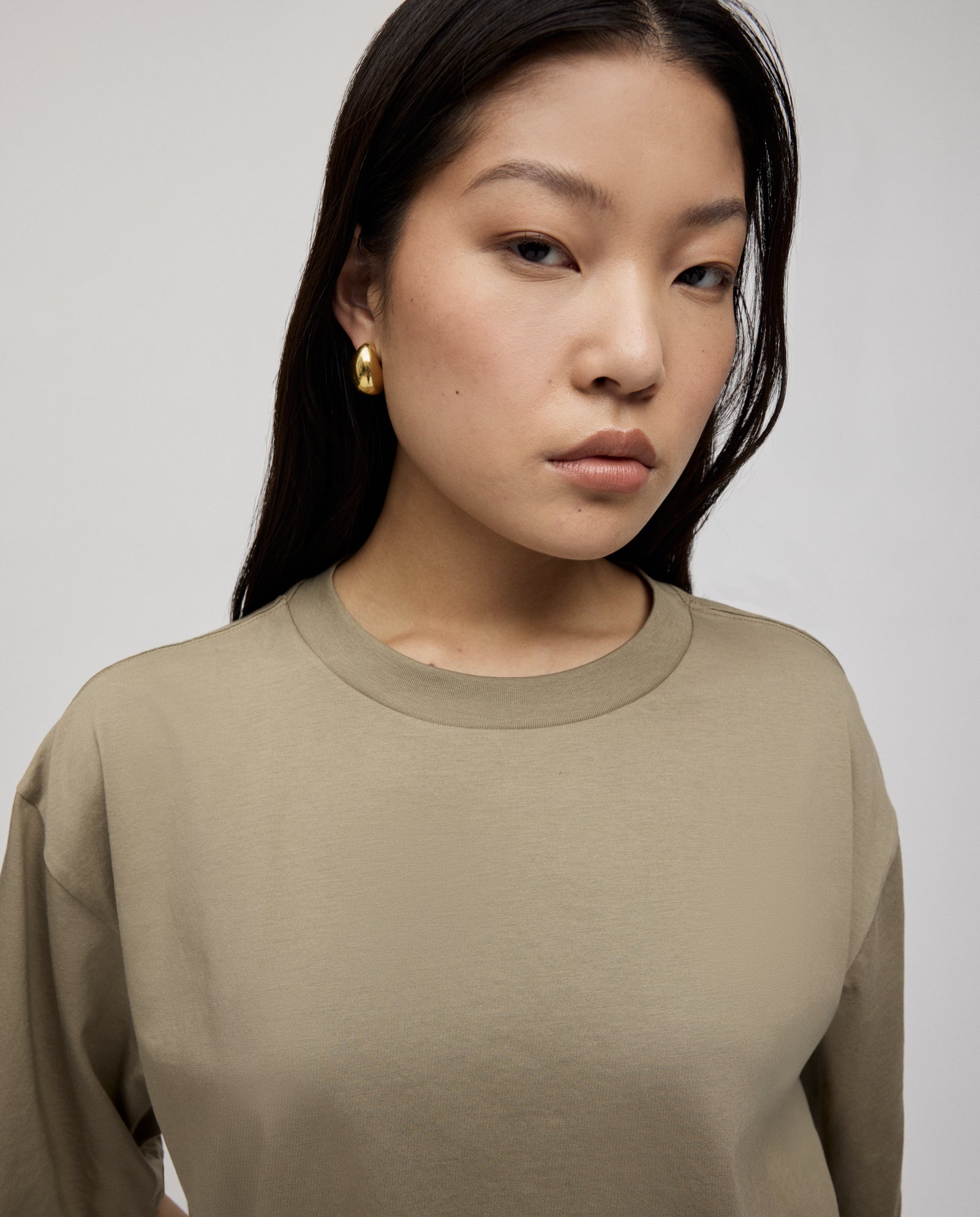 Woman with long dark hair wears an IVY OAK KYLA ROSE Top and gold hoop earrings, looking confidently at the camera.