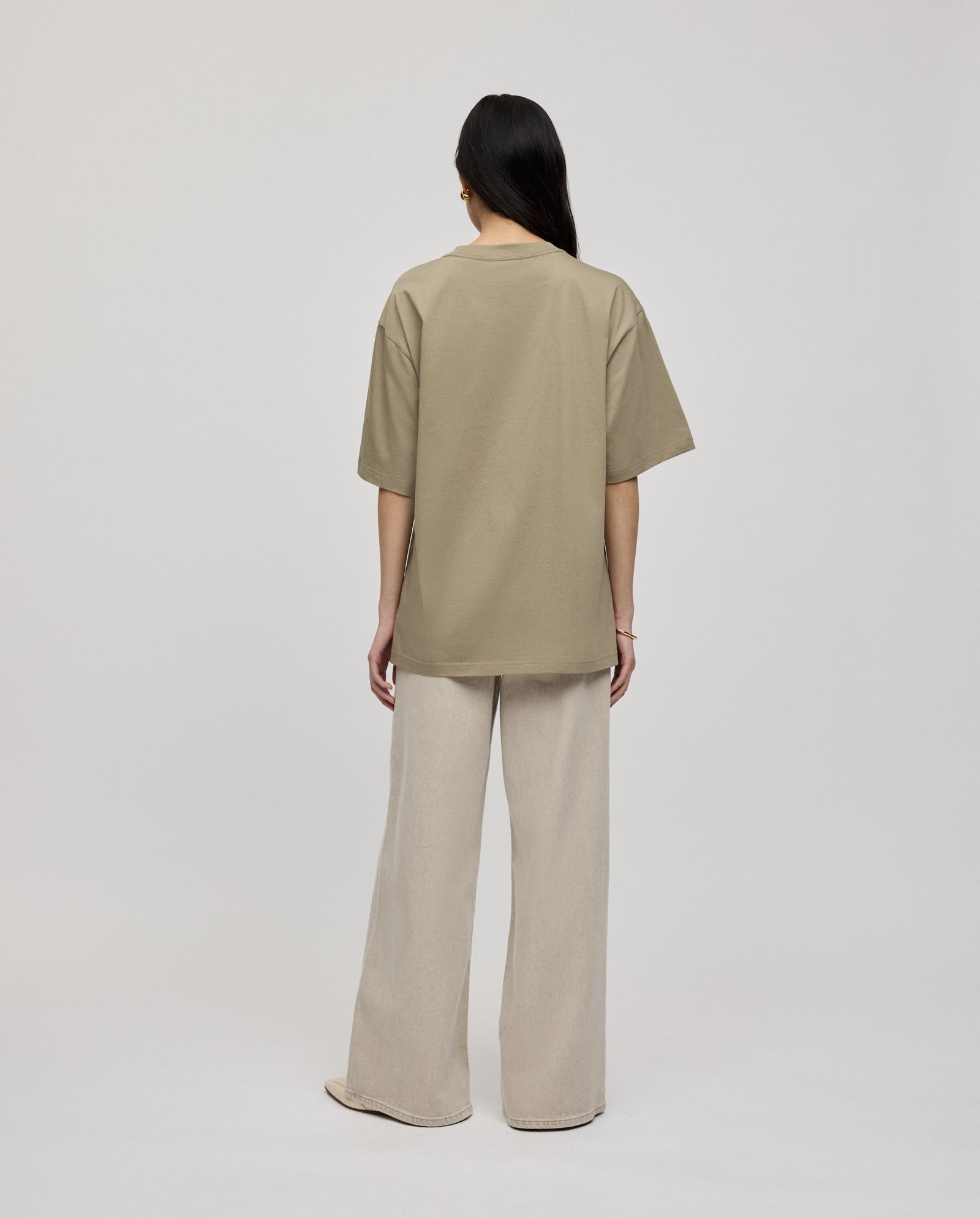A person stands facing away, wearing the ultra-soft KYLA ROSE Top by IVY OAK in beige with loose fit and wide-leg cream pants against a plain background.