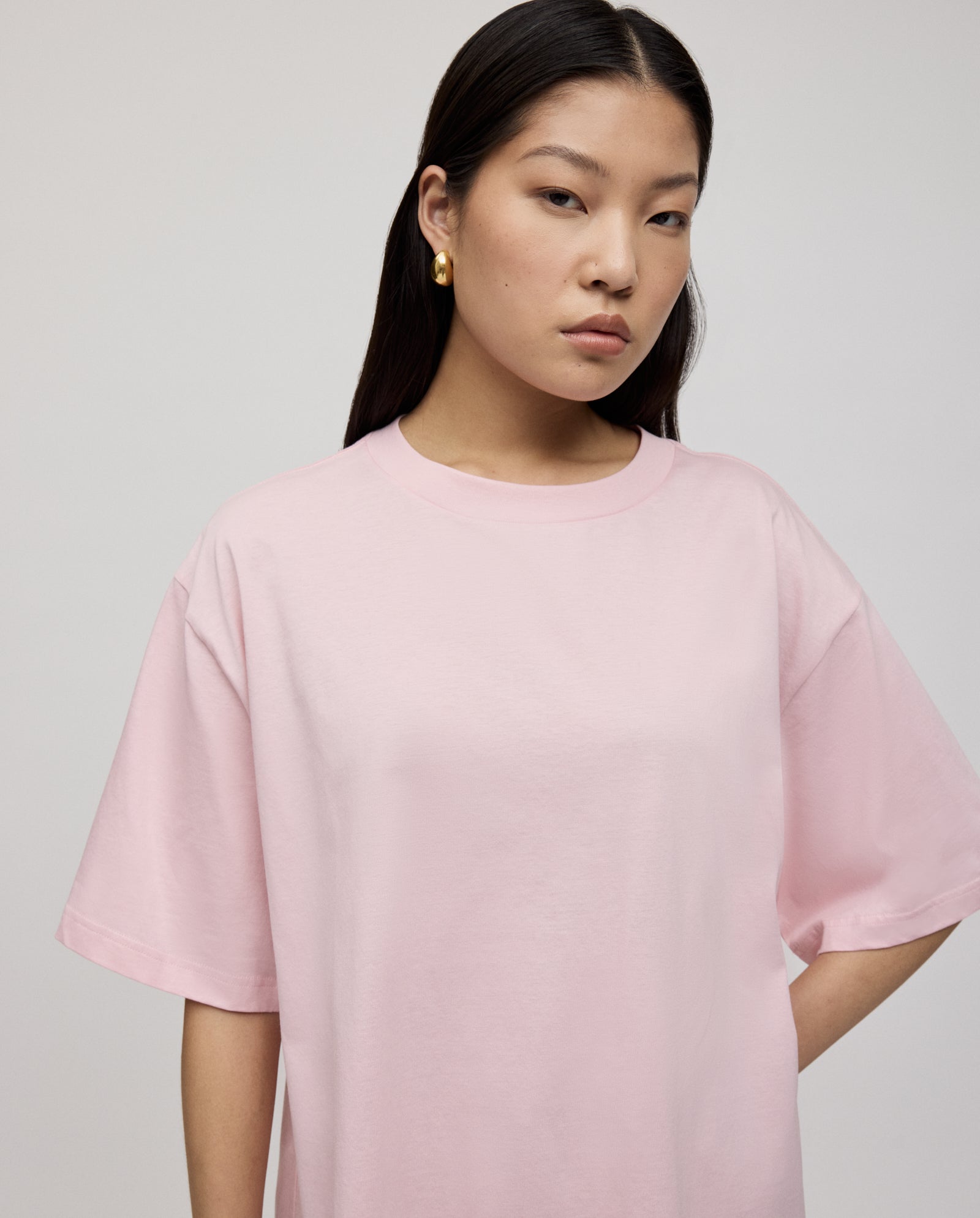 A woman with straight dark hair wears the IVY OAK KYLA ROSE Top, a loose fit, light pink boxy T-shirt, looking at the camera with a neutral expression.