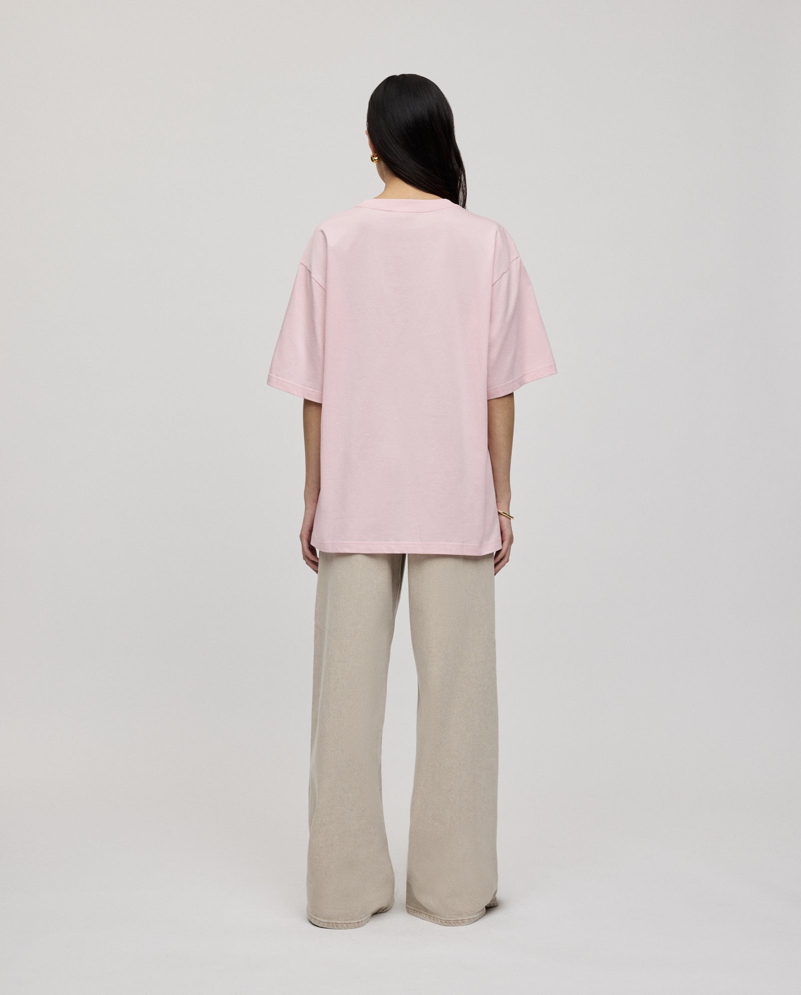 A person stands facing away in an ultra-soft, loose fit KYLA ROSE Top by IVY OAK in pink, paired with wide-leg beige pants against a plain background.