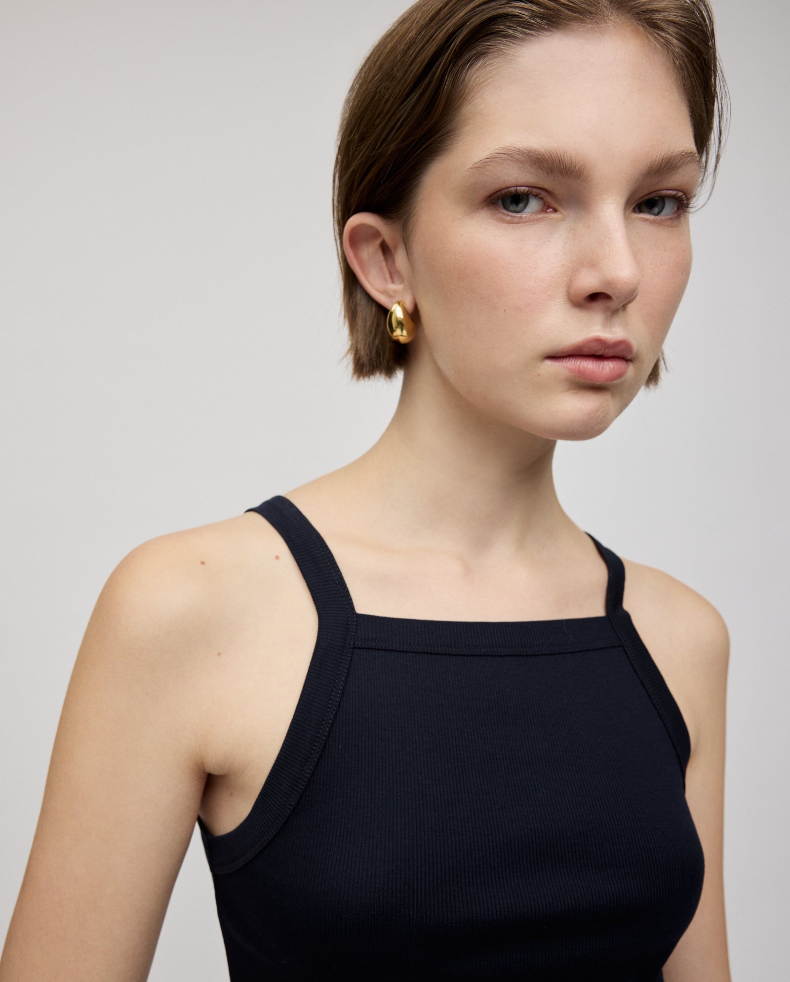Woman with short brown hair wears the IVY OAK KLARA ROSE Top and gold hoop earrings, looking at the camera with narrow shoulders.
