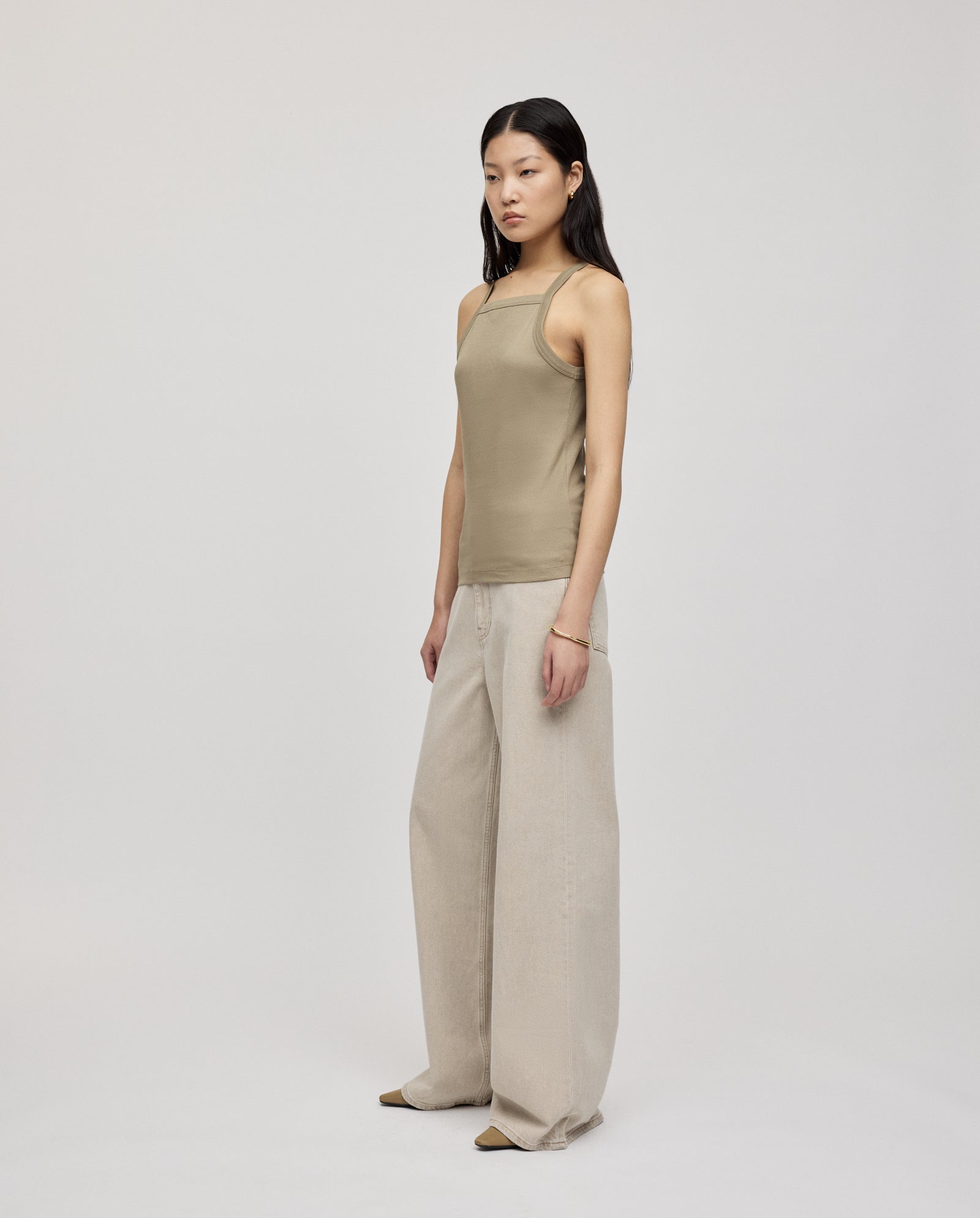 A woman wears the IVY OAK KLARA ROSE Top, a beige ripp-optic tank with narrow shoulders, paired with wide-leg cream pants, standing against a plain light background.