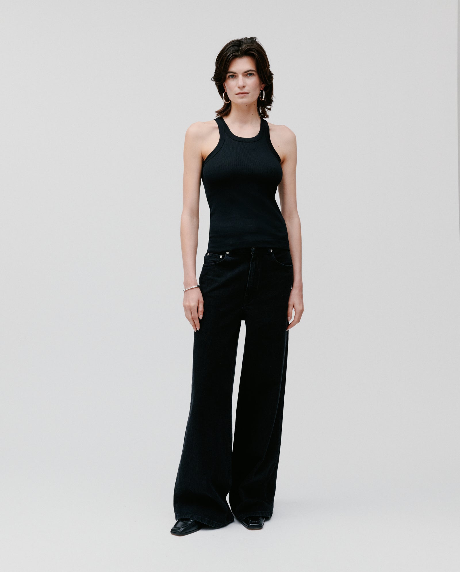Model wears the FINLEY Top by IVY OAK—a black ribbed tank—paired with wide-leg black pants, standing against a plain light background.