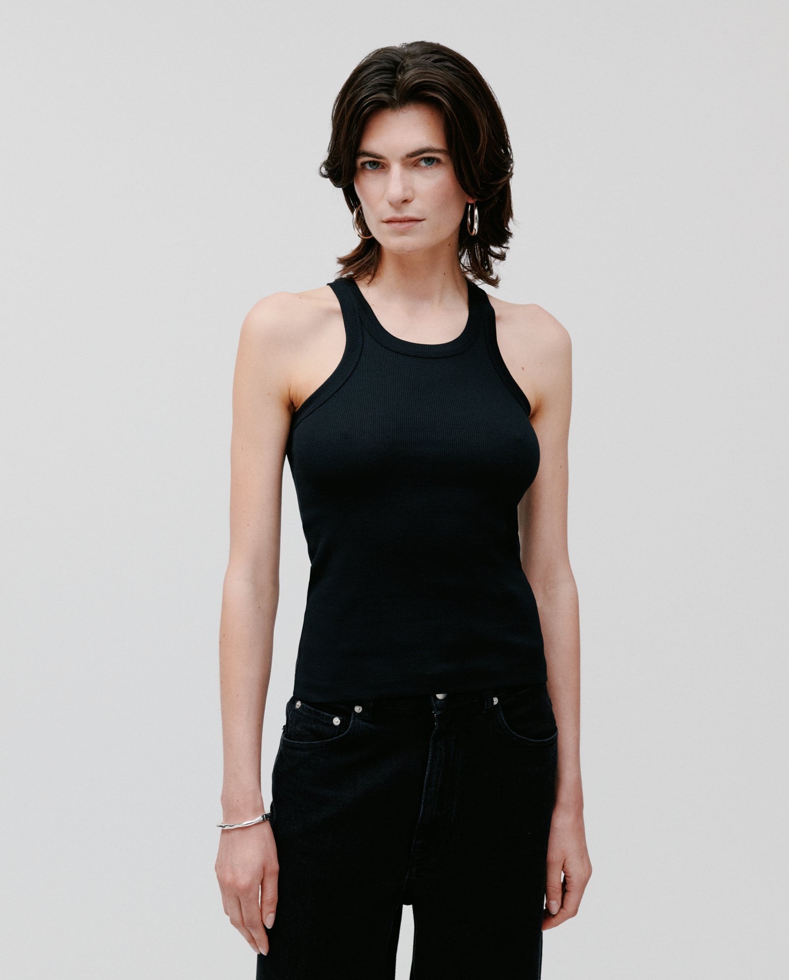 Person with short dark hair wears the IVY OAK FINLEY Top, a black fine knit tank, paired with black pants against a plain light background.