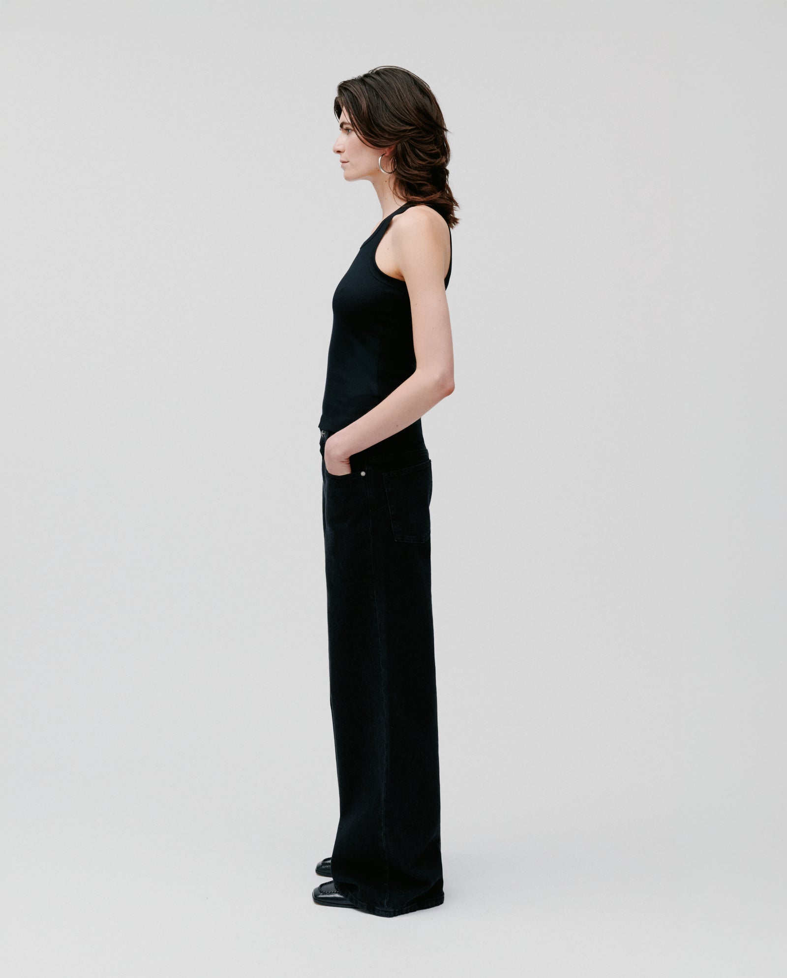 A woman in the FINLEY Top by IVY OAK, a black ribbed tank, and wide-leg pants stands in profile against a plain white background.