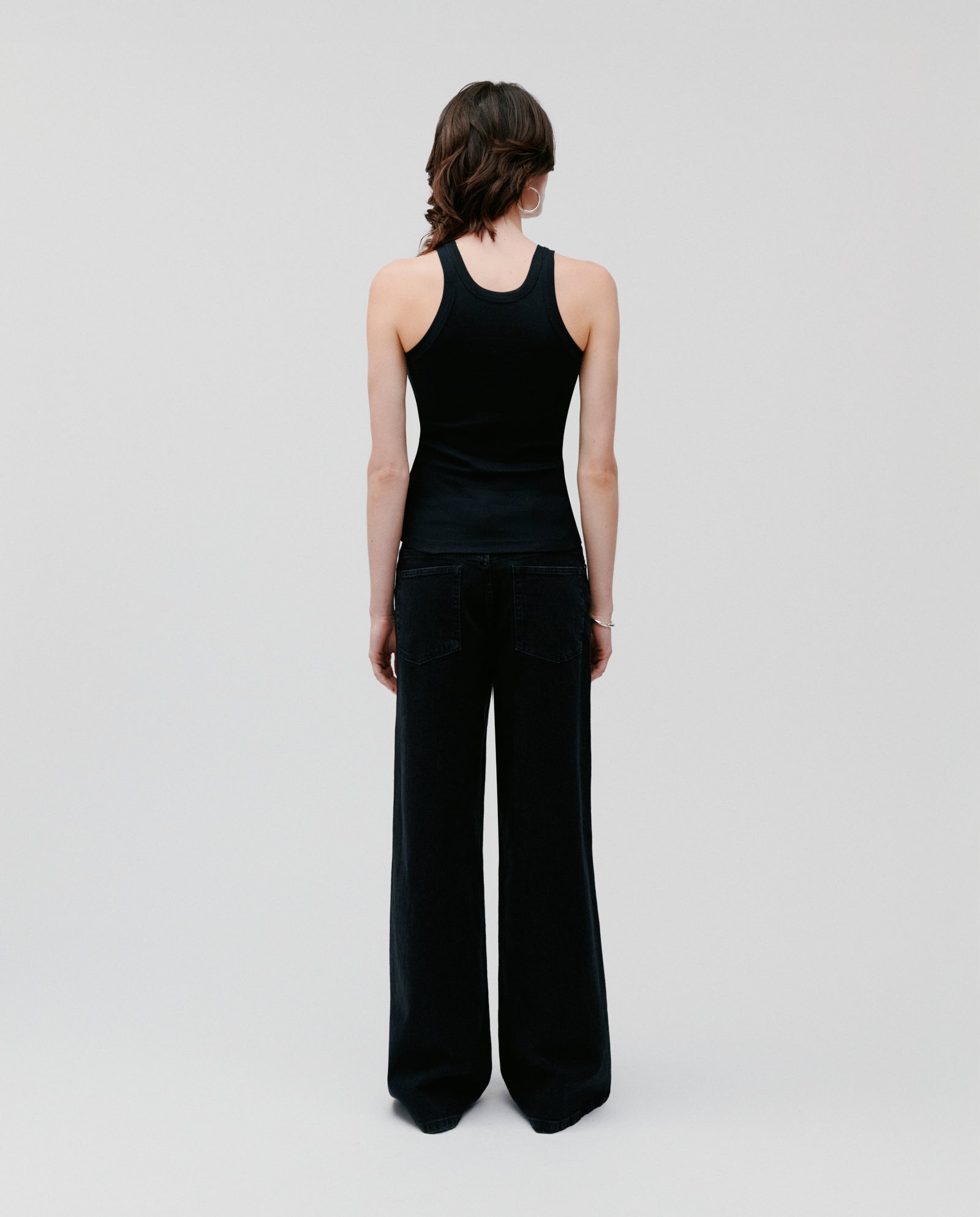 A person faces away from the camera, wearing the IVY OAK FINLEY ribbed tank top and wide-leg black pants against a plain background.