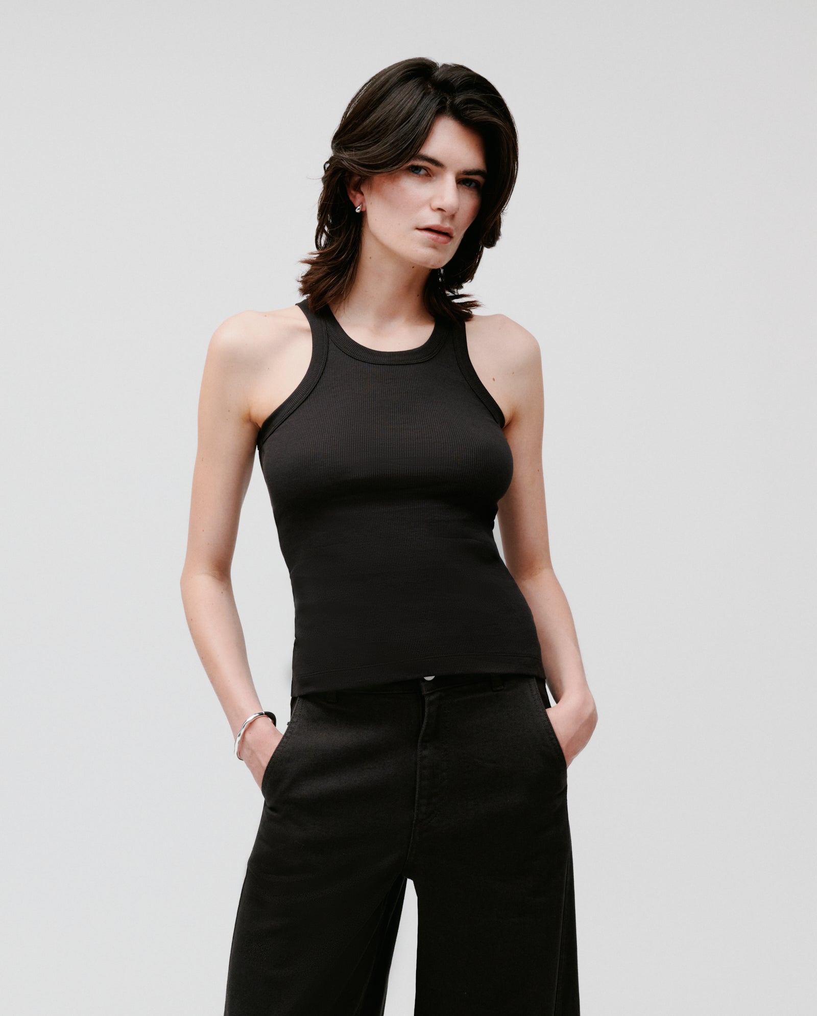 Person with short dark hair wearing the IVY OAK FINLEY black ribbed knit sleeveless top and black pants, standing against a plain background.